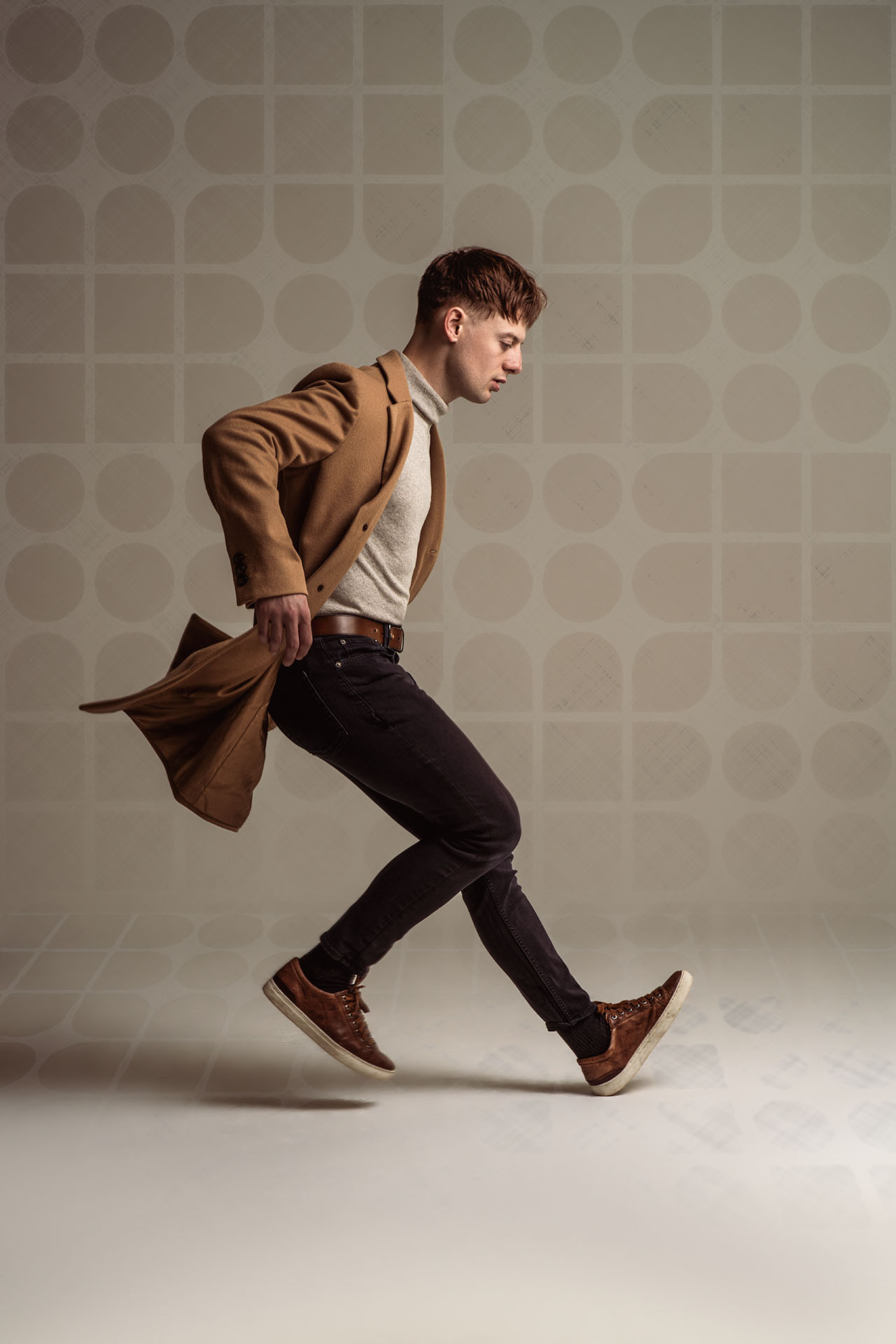 Male model captured mid-stride with a tan coat swinging off one shoulder, dynamic editorial photography