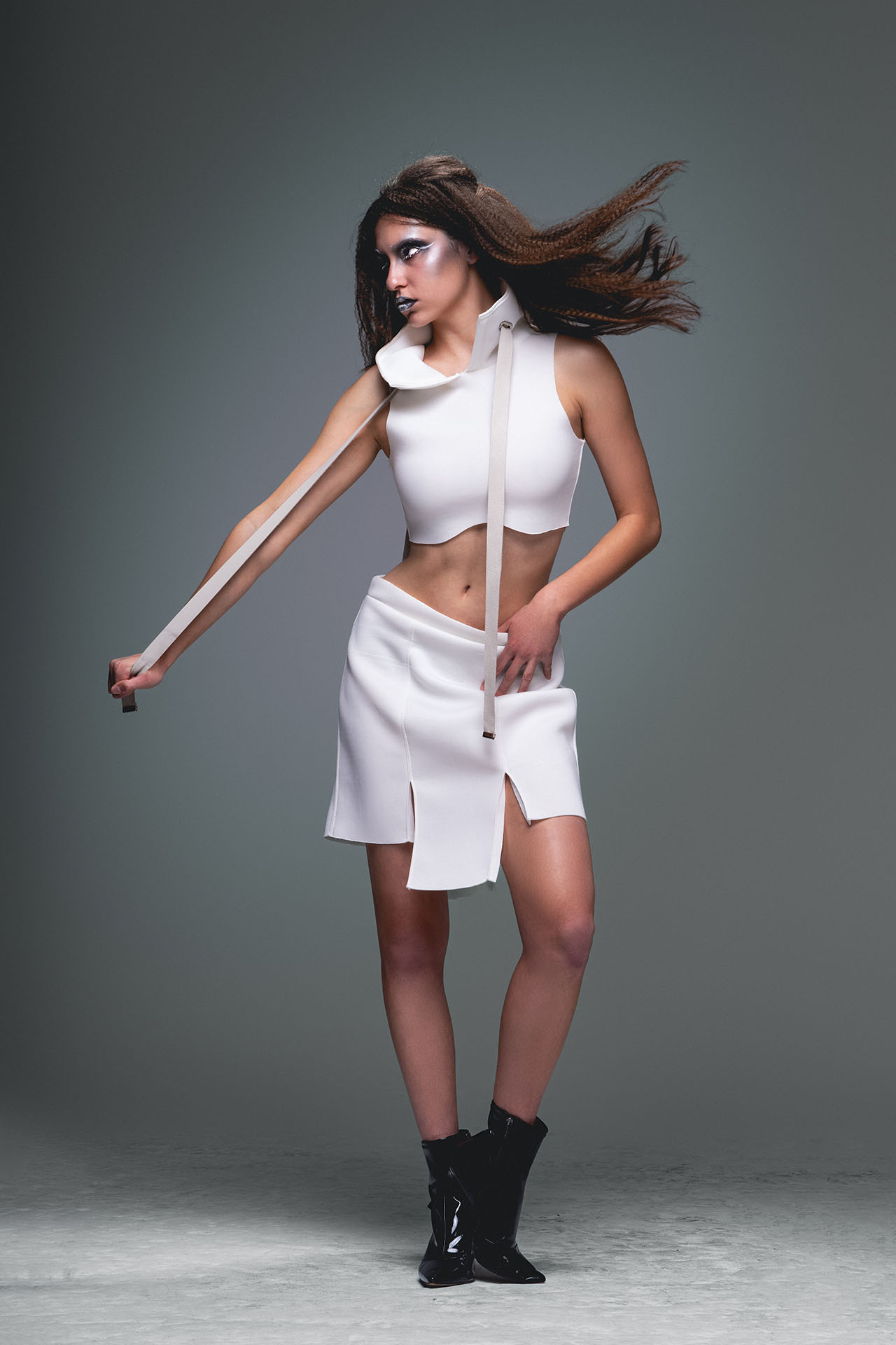 Model in a white cropped top and asymmetrical skirt with hair captured in dynamic motion, one arm extended