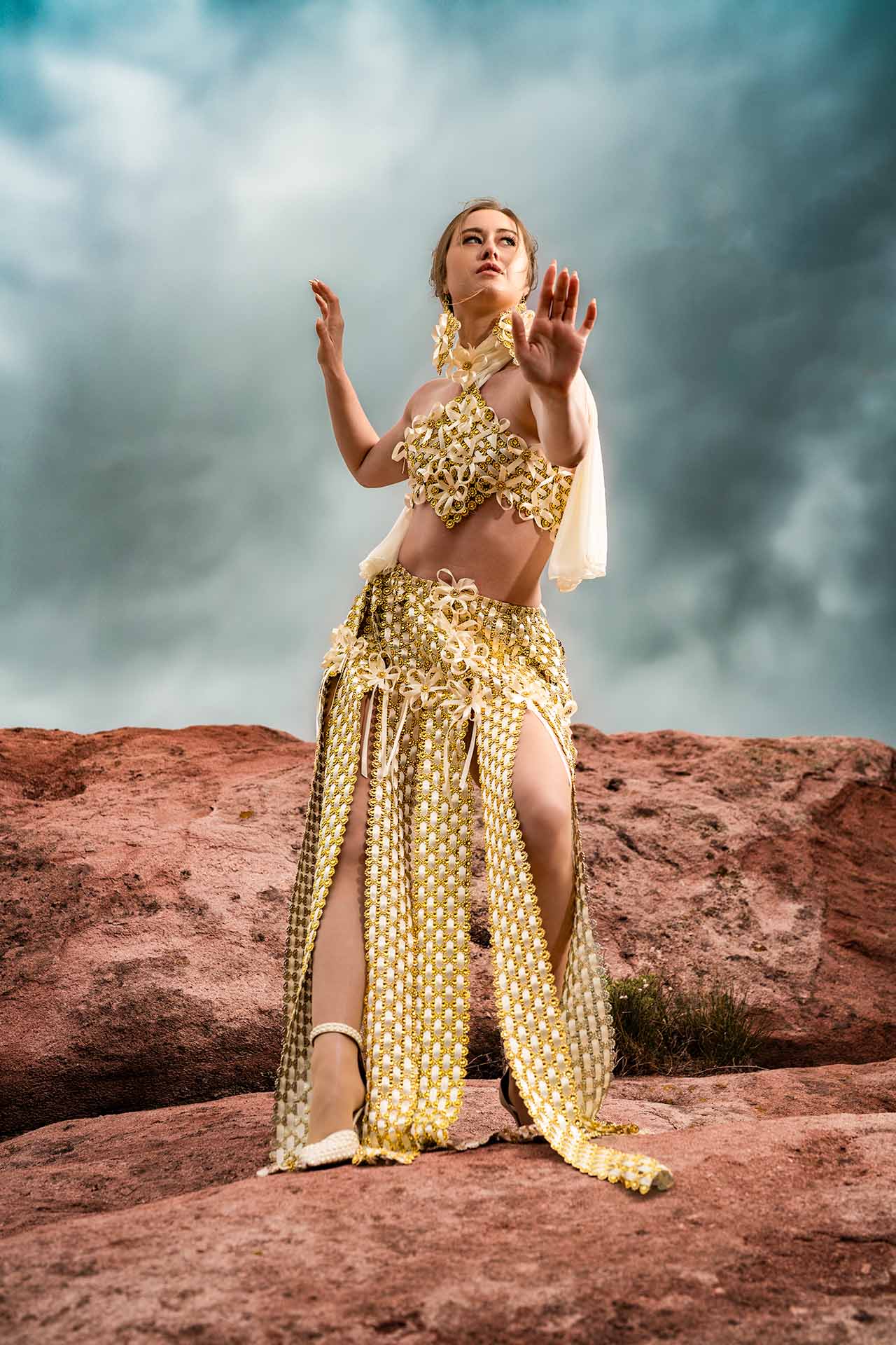 Model in a gold top and skirt posing on red rock formations, desert editorial fashion photography