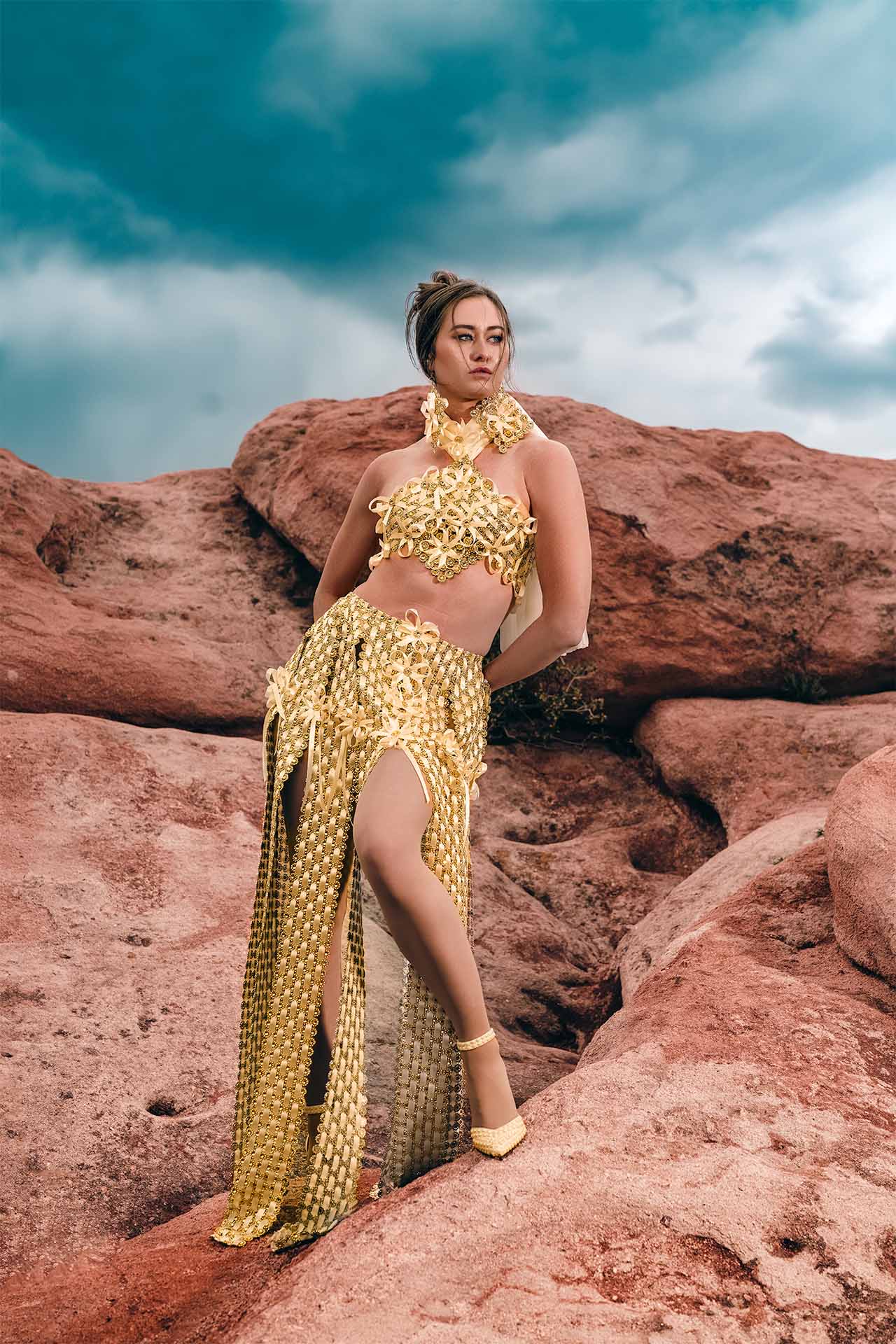 Model in a gold outfit posing among red rock formations, alternate desert editorial photography