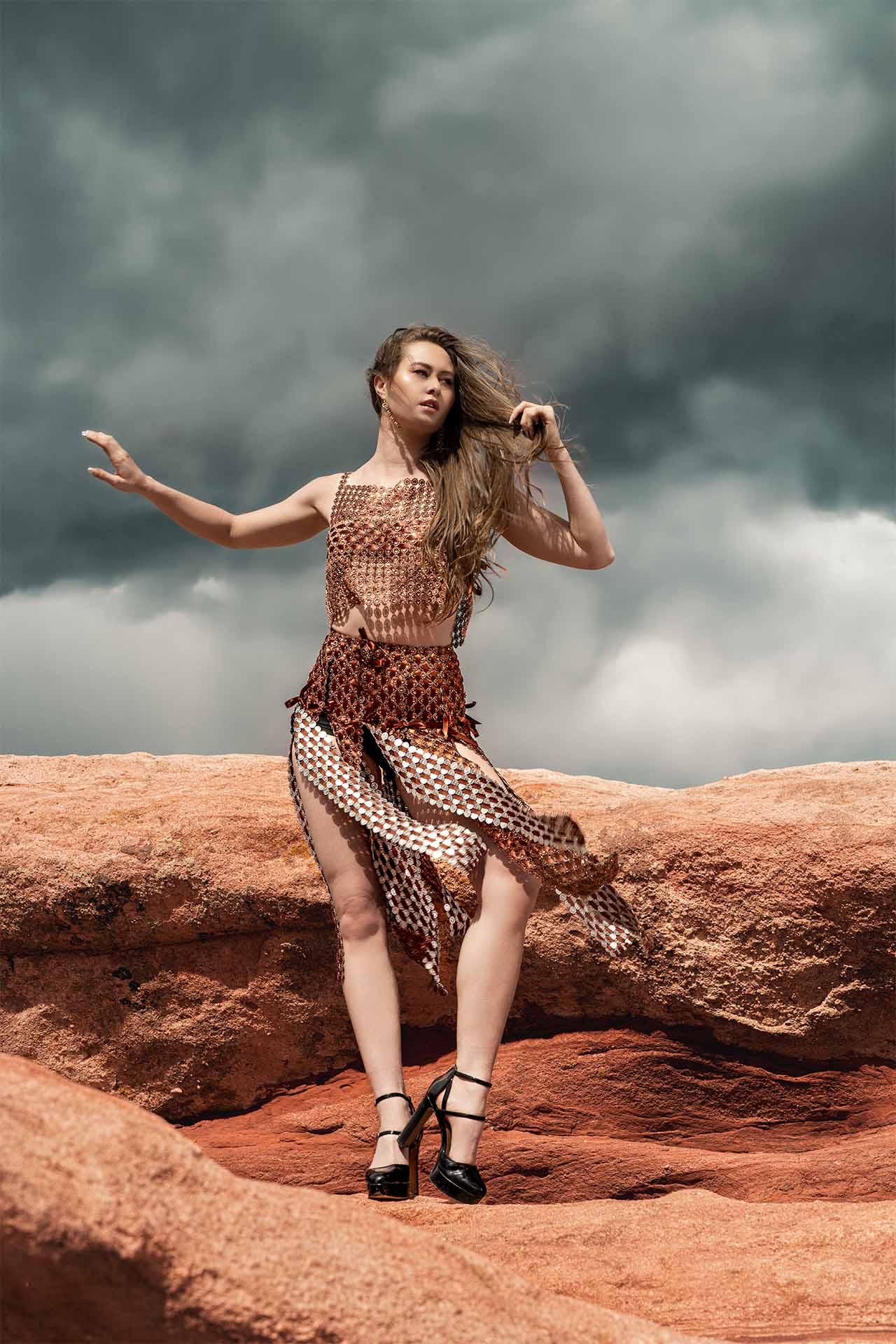 Model in a copper outfit posing dynamically on red rock formations, desert editorial photography