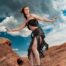 Model in a black top and skirt posing dynamically on red rock formations, desert editorial photography