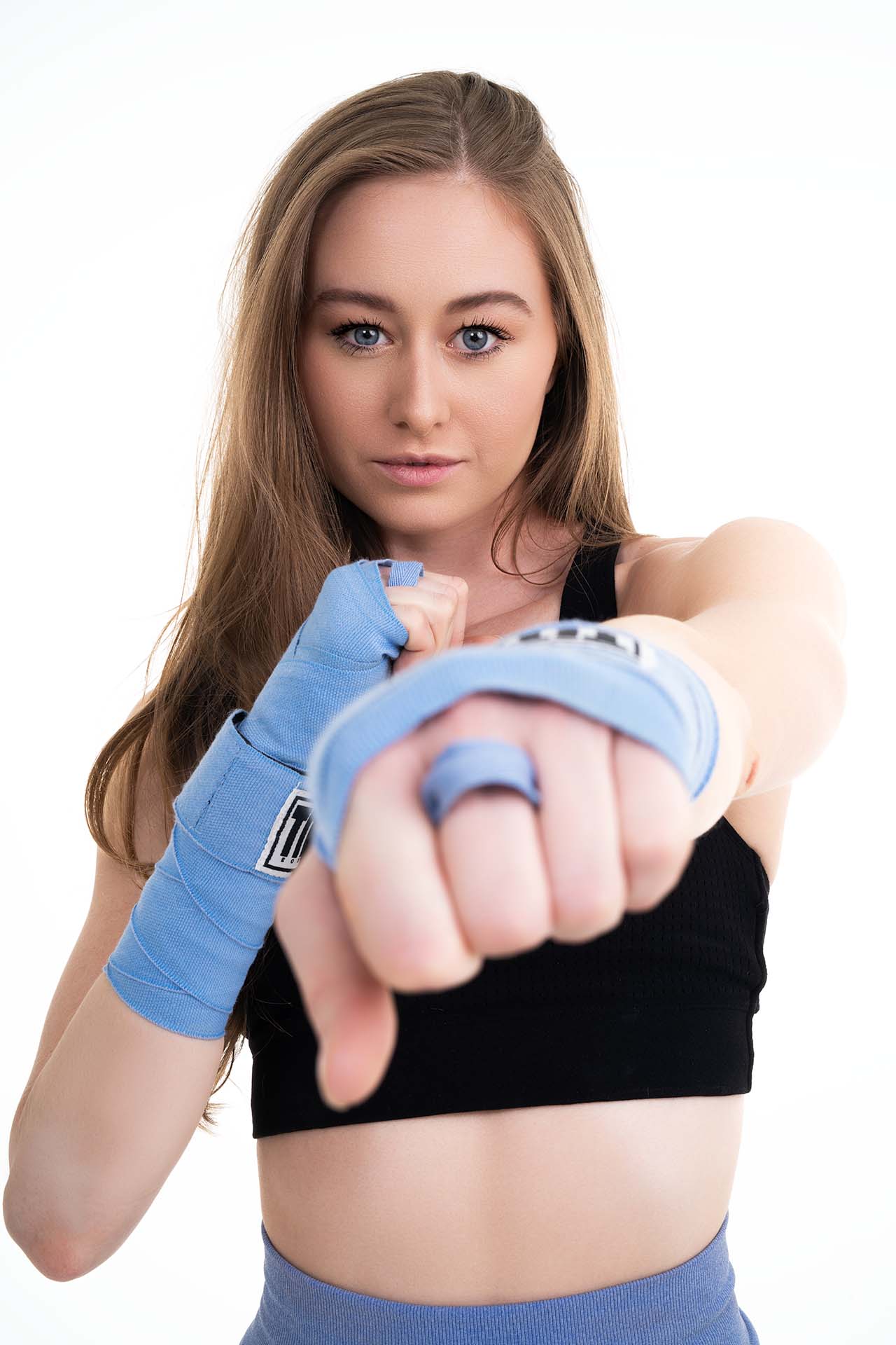 Model in activewear and boxing wraps throwing a punch toward the camera, fitness studio photography