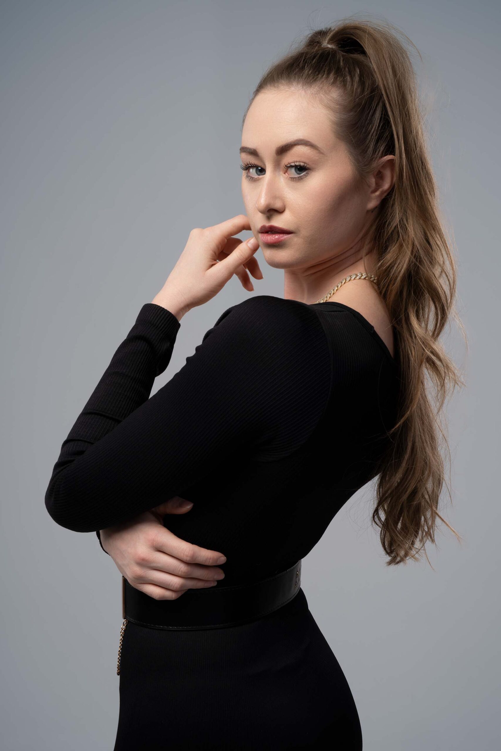 Model in a black outfit with a gold chain belt, standing studio catalog photography