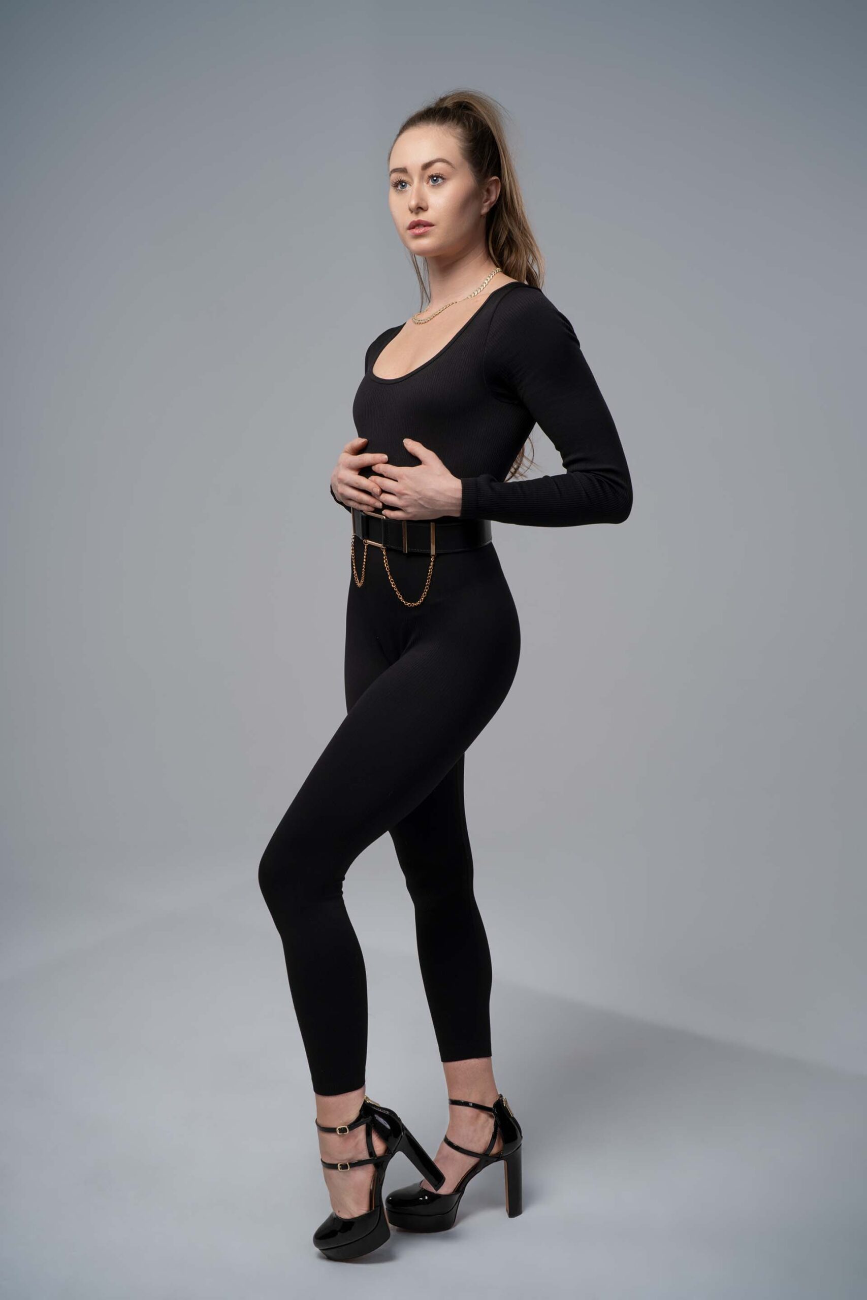 Model in a black outfit with a gold chain belt, alternate standing pose