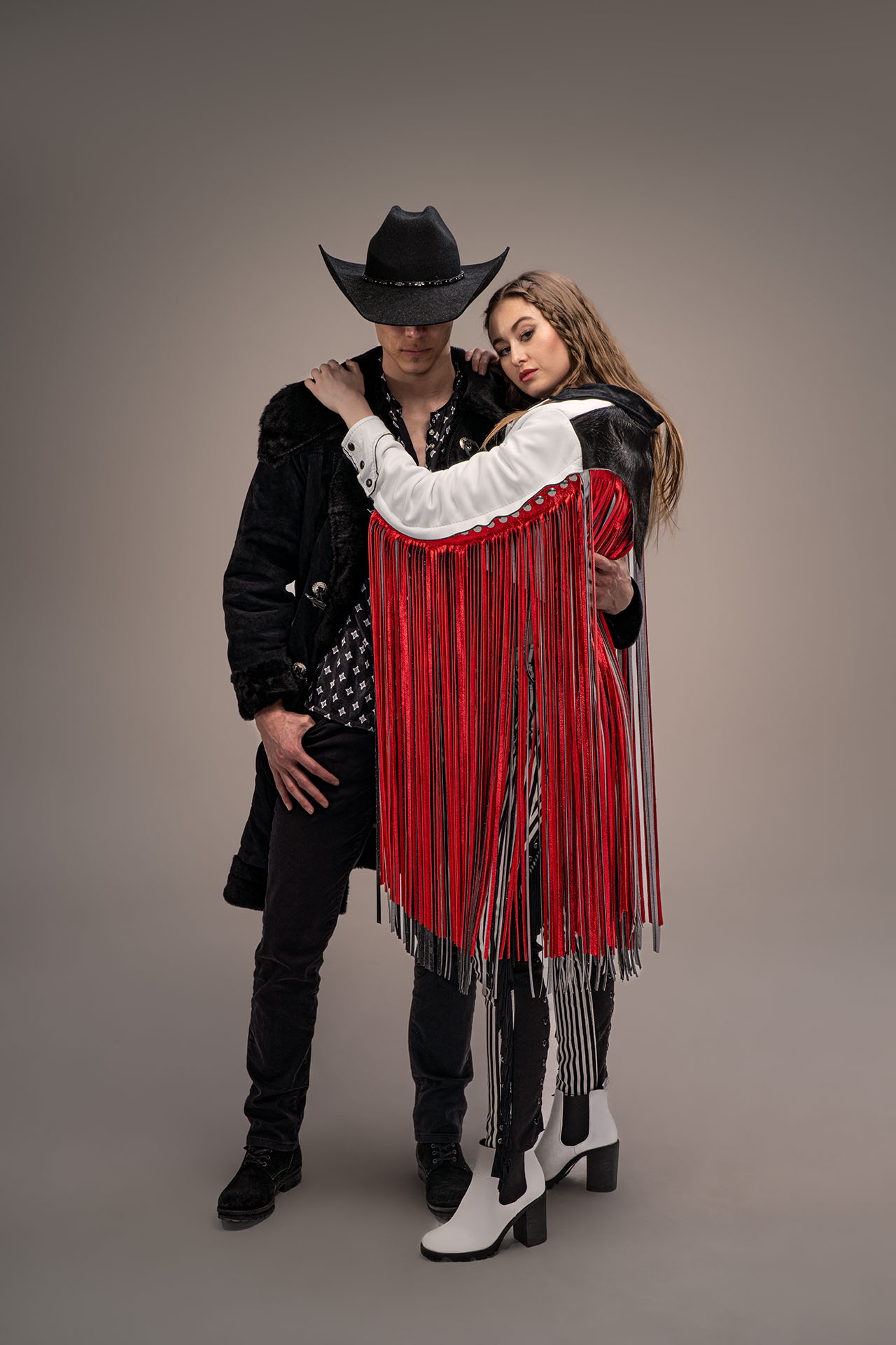 Man in a cowboy hat embracing a woman in a red and white fringe outfit, western-themed duo editorial photography