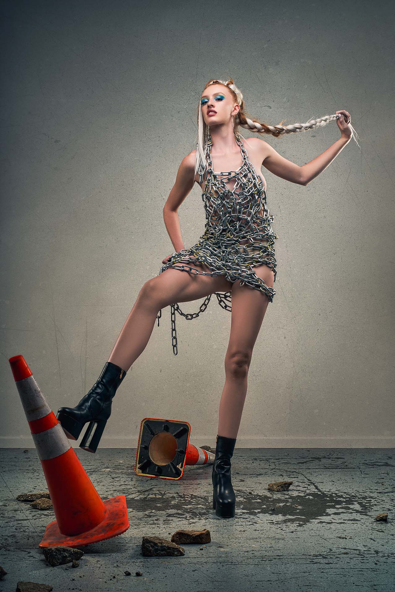 Model in a chain-link dress with two overturned traffic cones on the ground, dynamic avant-garde editorial photography