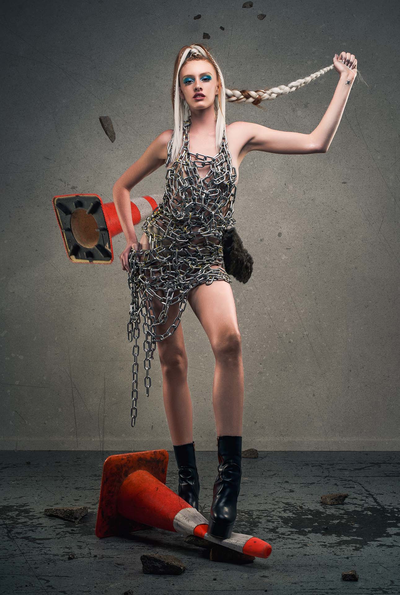 Model in a chain-link dress with a knocked-over traffic cone, dynamic hair movement, avant-garde editorial photography
