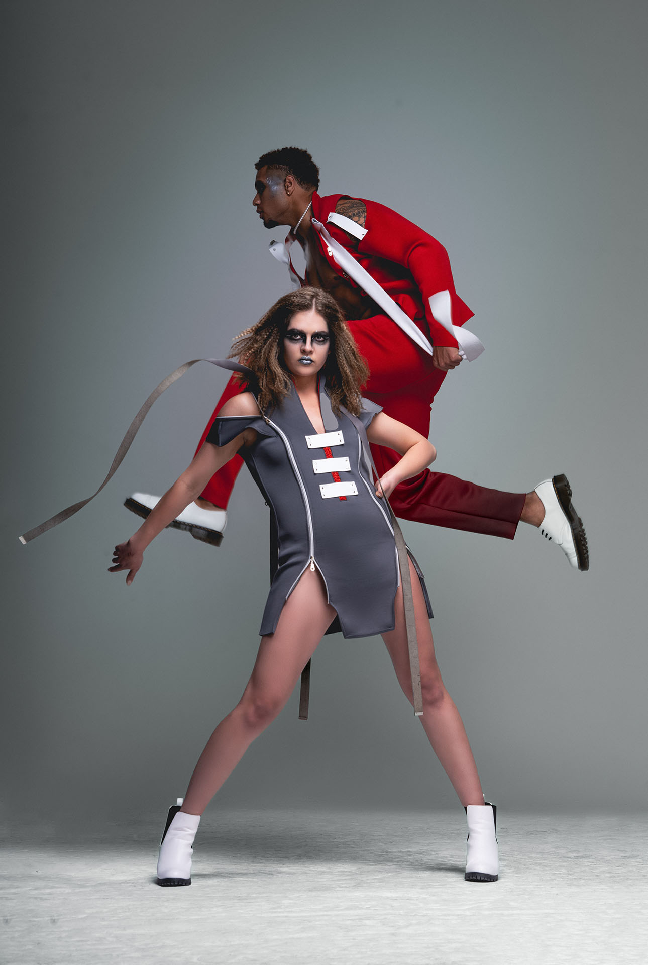Two models, one in a white top standing and one in a red jumpsuit seated, studio fashion photography