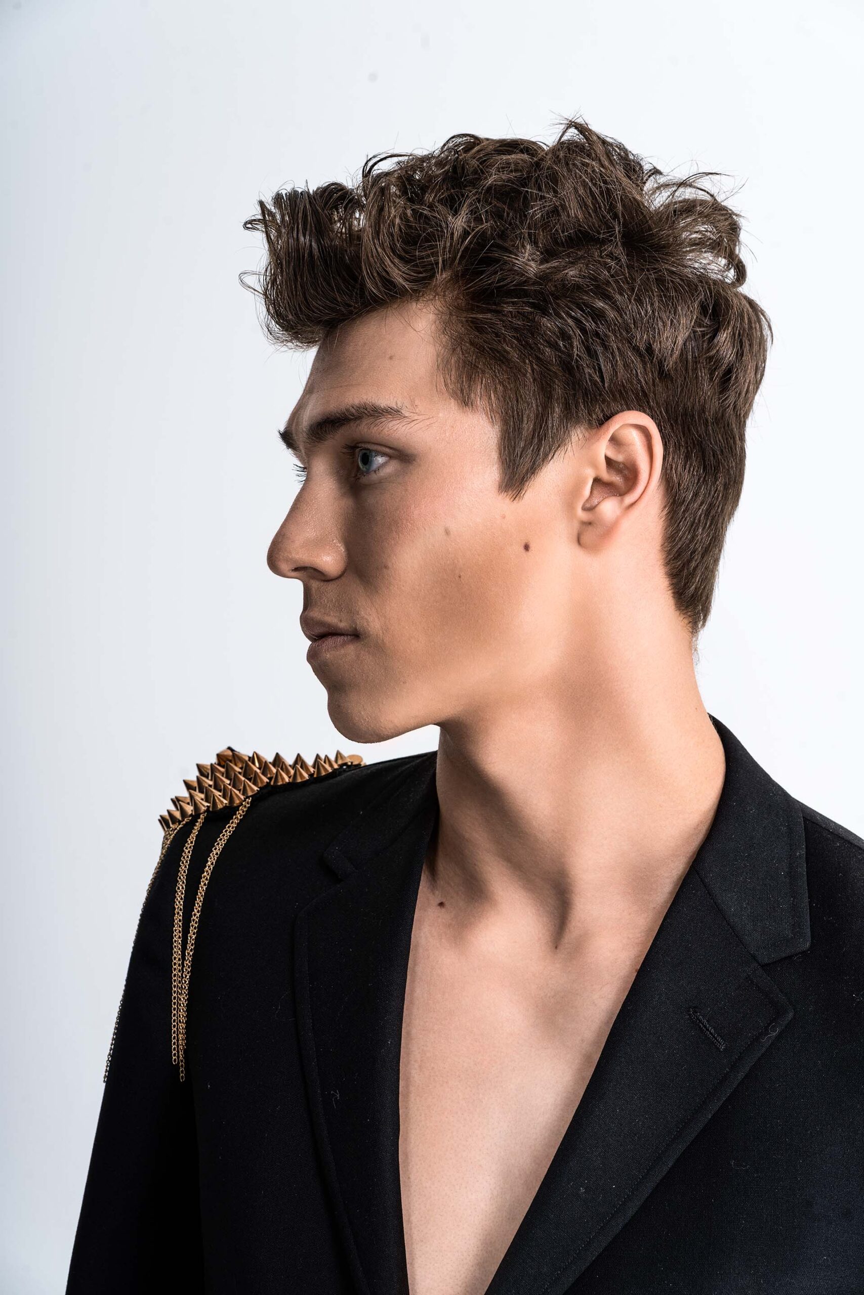 Profile portrait of a model in an open black blazer with a decorative gold spiked chain draped over one shoulder
