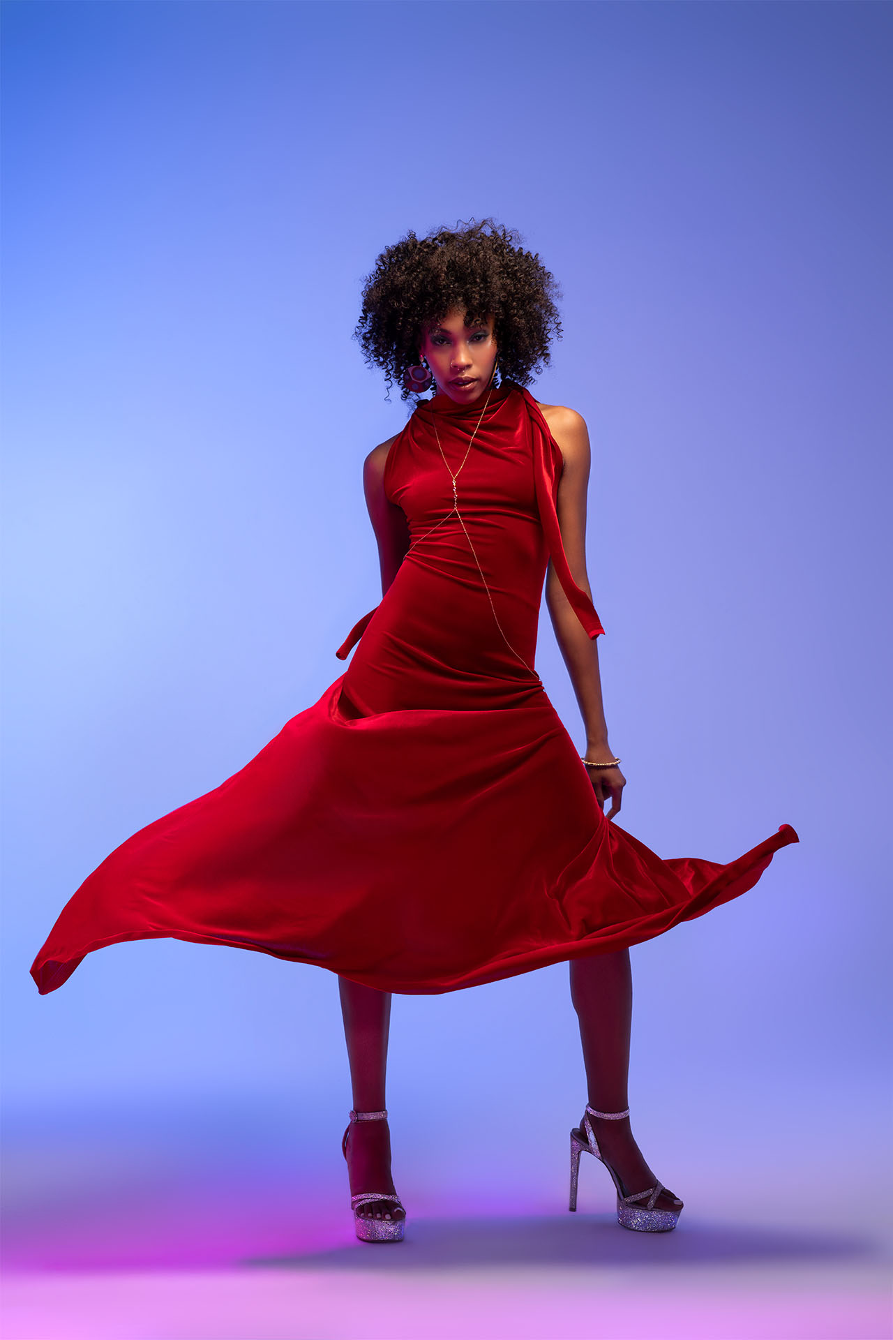 Model in a red dress with layered jewelry, editorial studio portrait