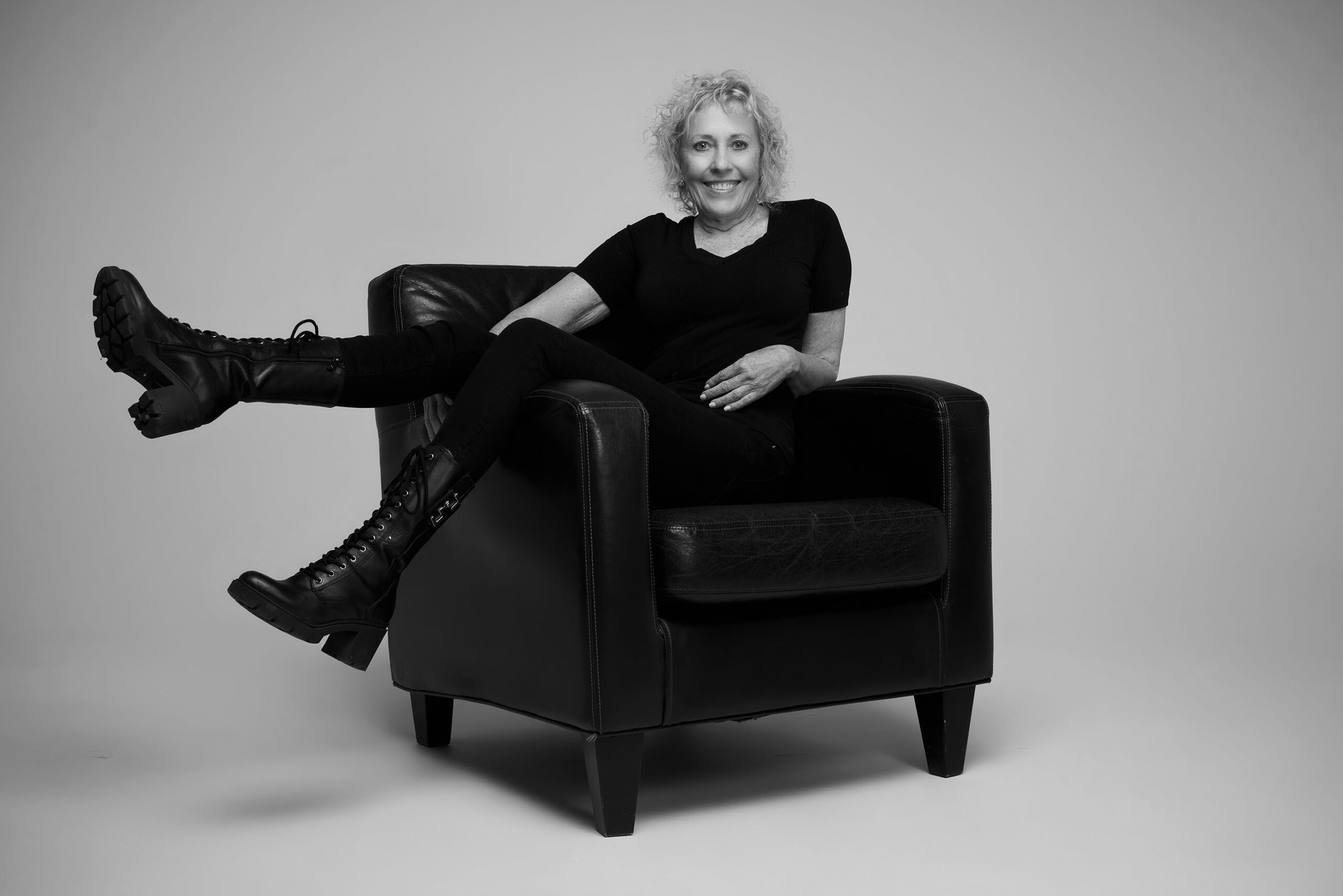 Black-and-white portrait of a woman with curly hair seated in a leather chair