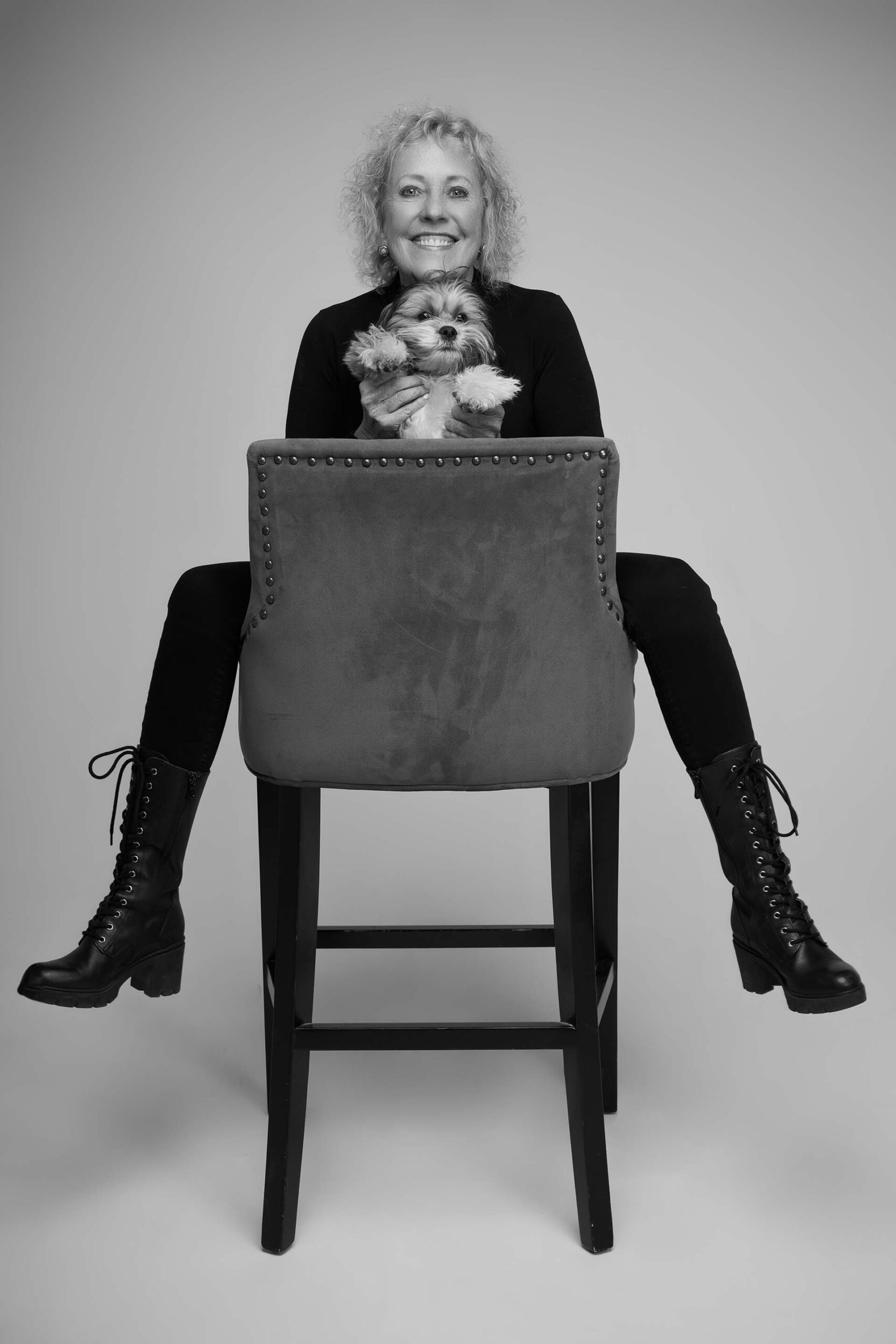 Black-and-white portrait of a woman seated backwards on a stool with arms crossed on the backrest