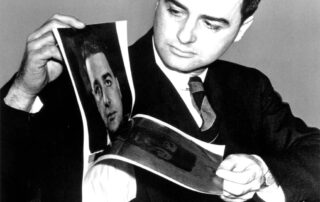 Archival-style black-and-white photo of a man in a suit looking at printed photographs