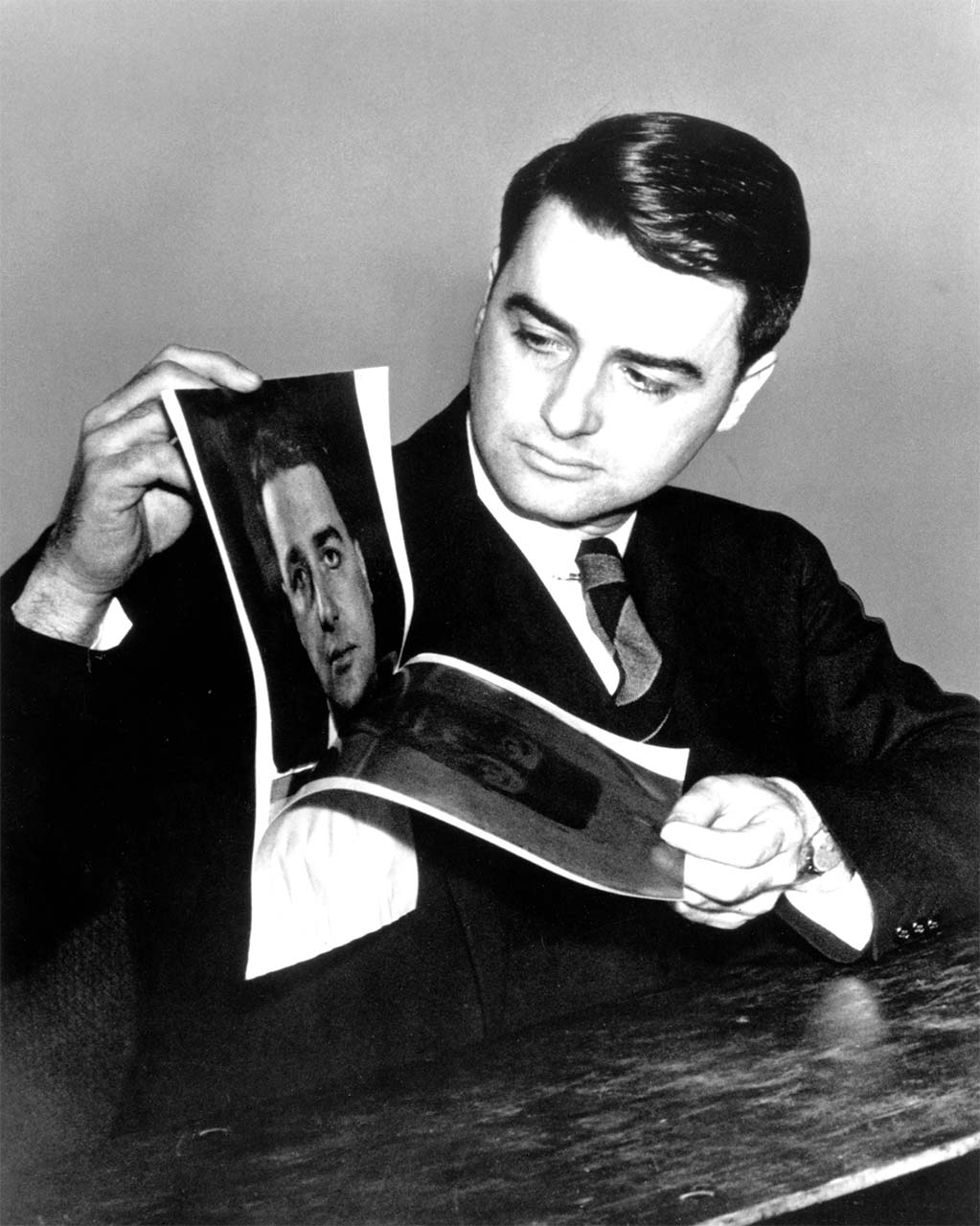 Archival-style black-and-white photo of a man in a suit looking at printed photographs