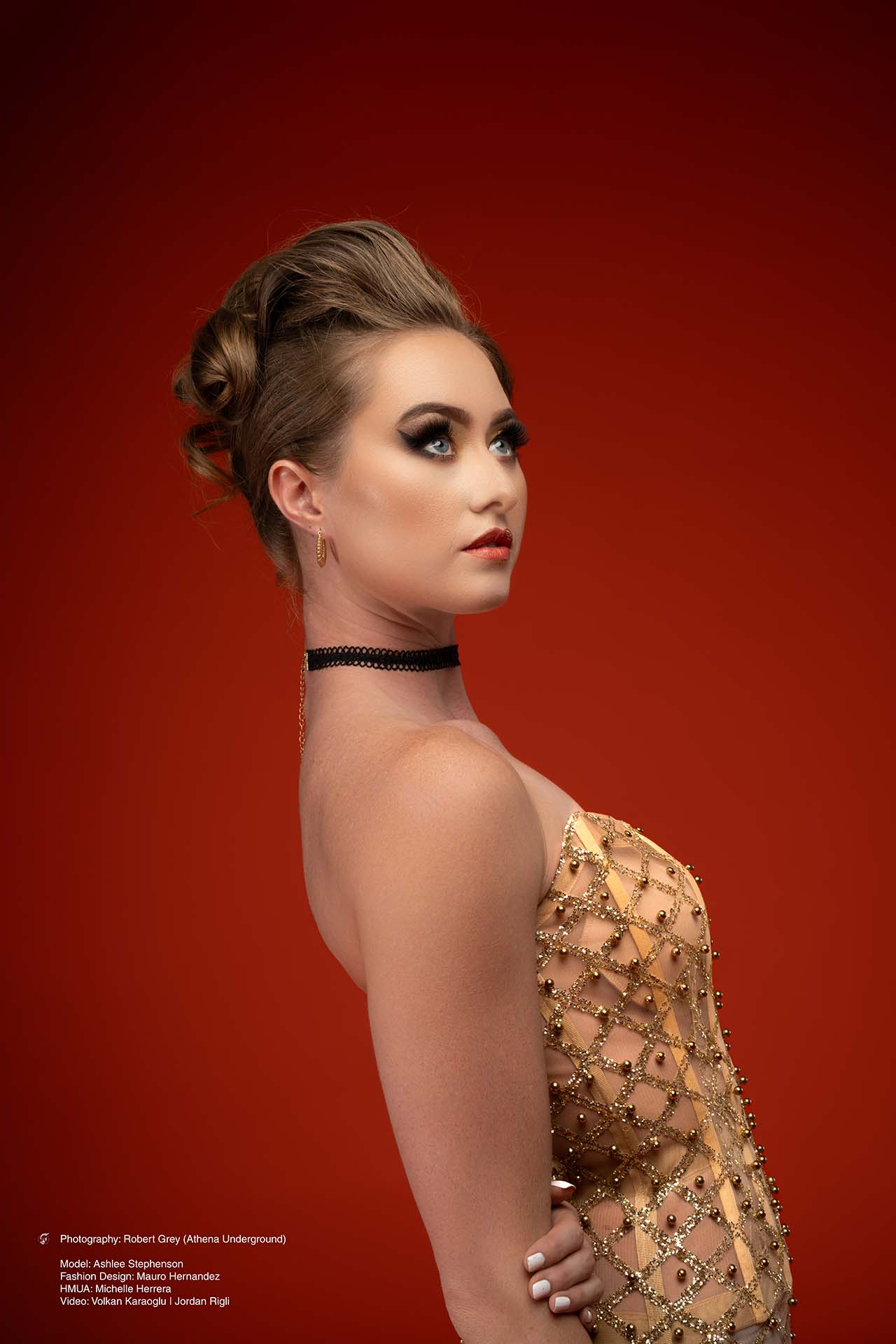 Model in a gold corset gown in side profile against a red studio backdrop