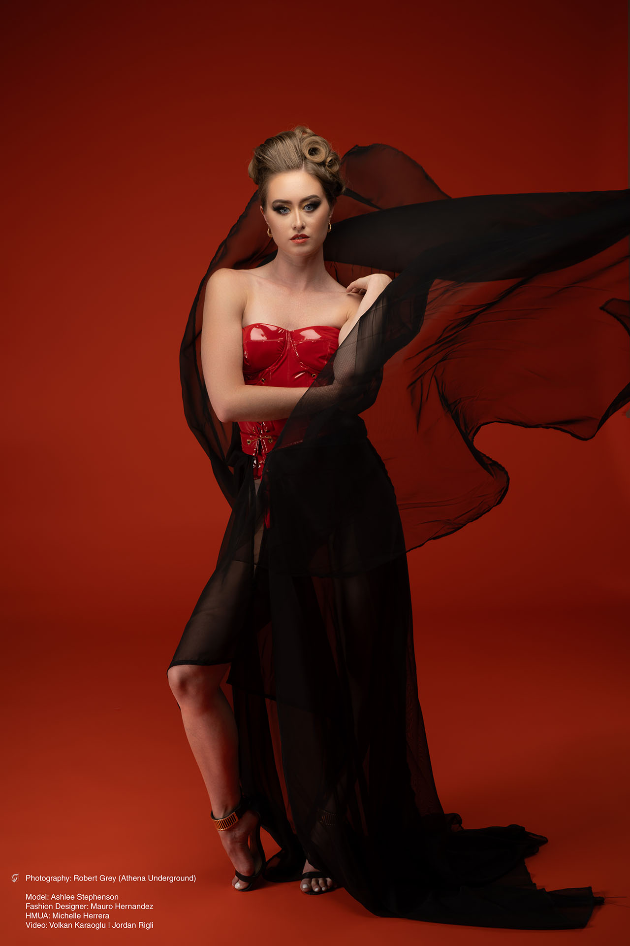 Model in a red corset with a flowing black skirt and veil against a red studio backdrop