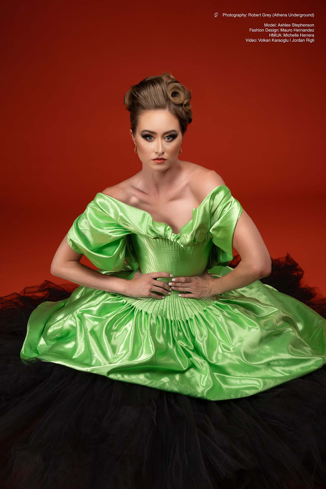 Model in a green satin puff-sleeve gown seated against a red studio backdrop