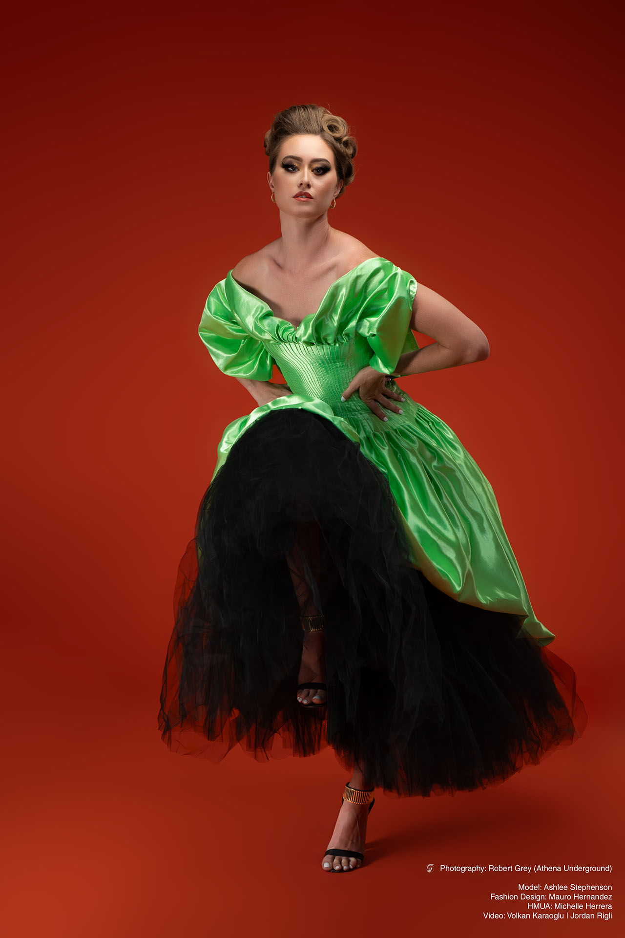 Model in a green and black gown captured mid-movement against a red studio backdrop