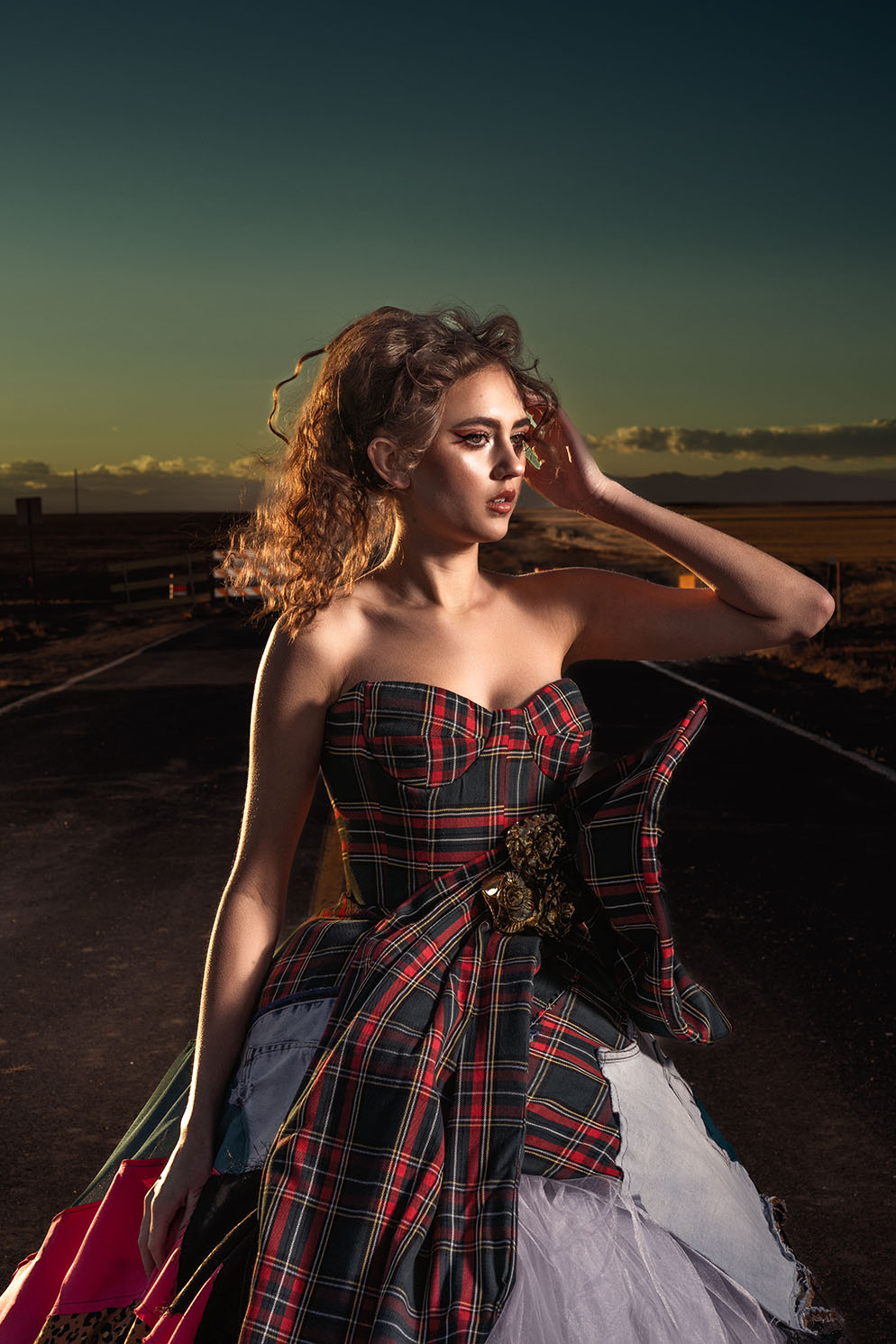 Model in a plaid corset top and skirt, full-length portrait on a deserted road at dusk