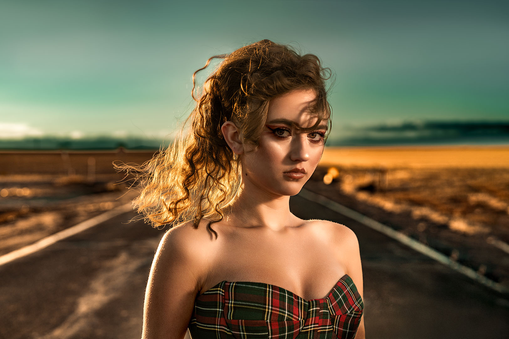 Model in a plaid corset top standing on a deserted road under a dusk sky, editorial photography