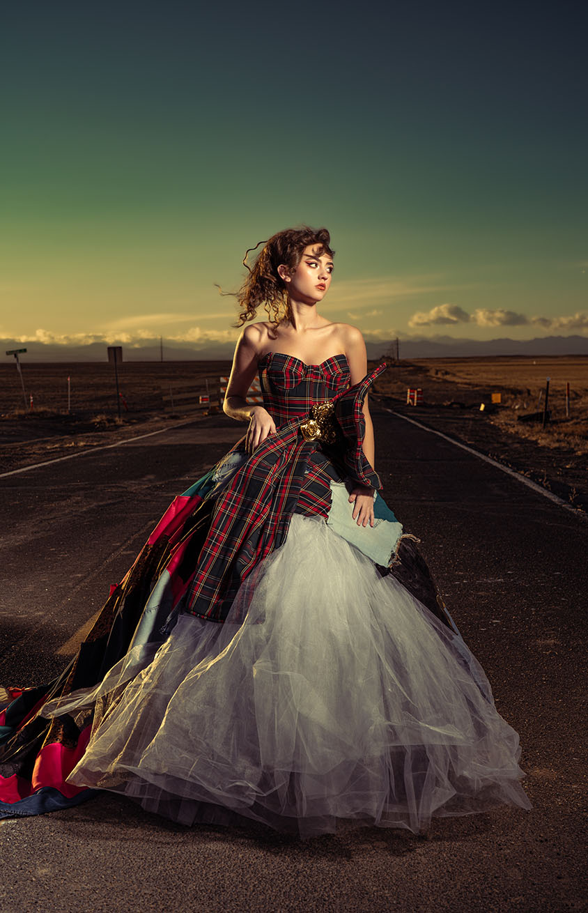 Model in a plaid corset ball gown standing on a deserted road, alternate pose at sunset