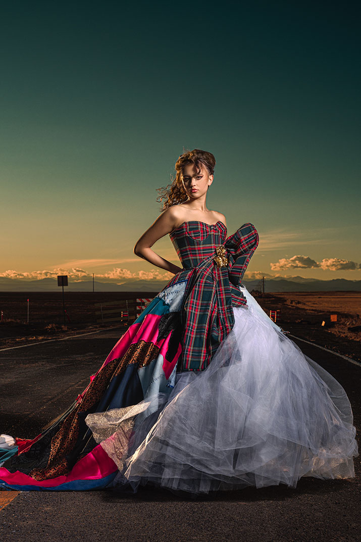 Model in a plaid corset ball gown, side pose on a deserted road at sunset