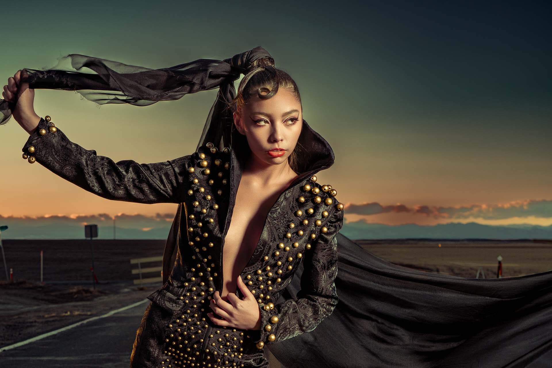 Studded Veil Editorial Photography 01 Model in a black studded outfit with a flowing black veil on a deserted road at sunset