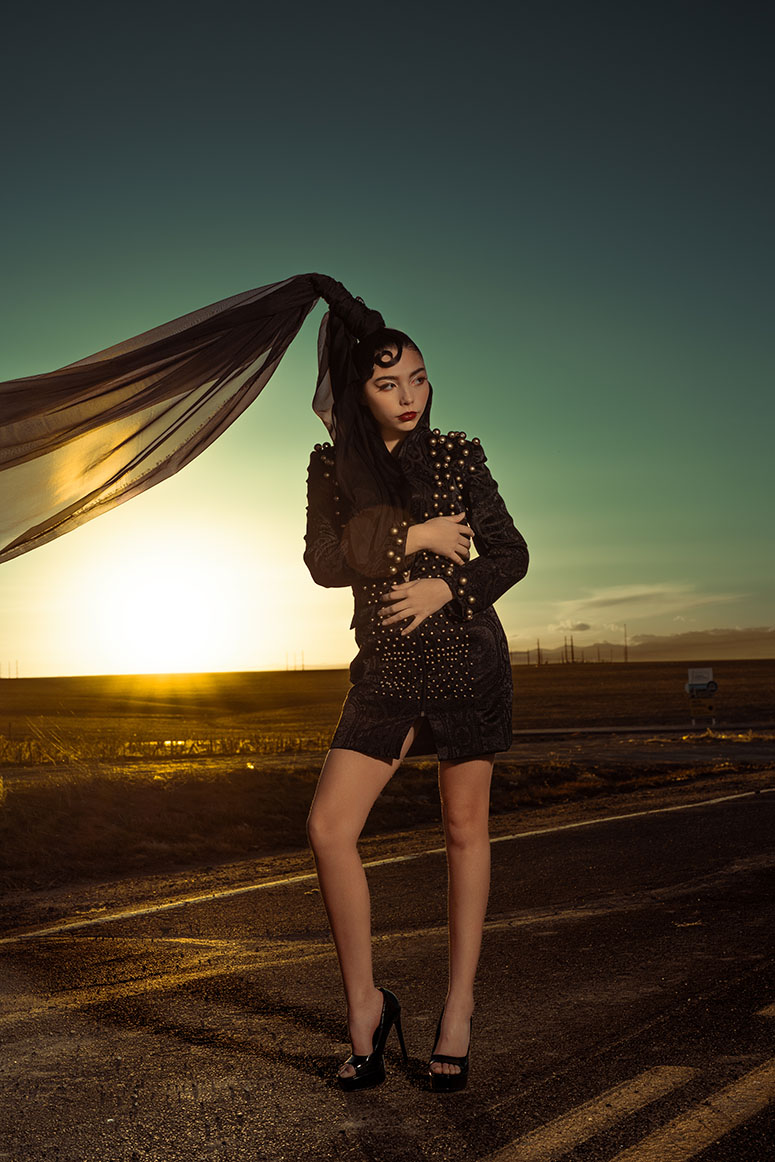 Studded Veil Editorial Photography 03 Model with a black veil flowing horizontally in the wind on a deserted road at sunset