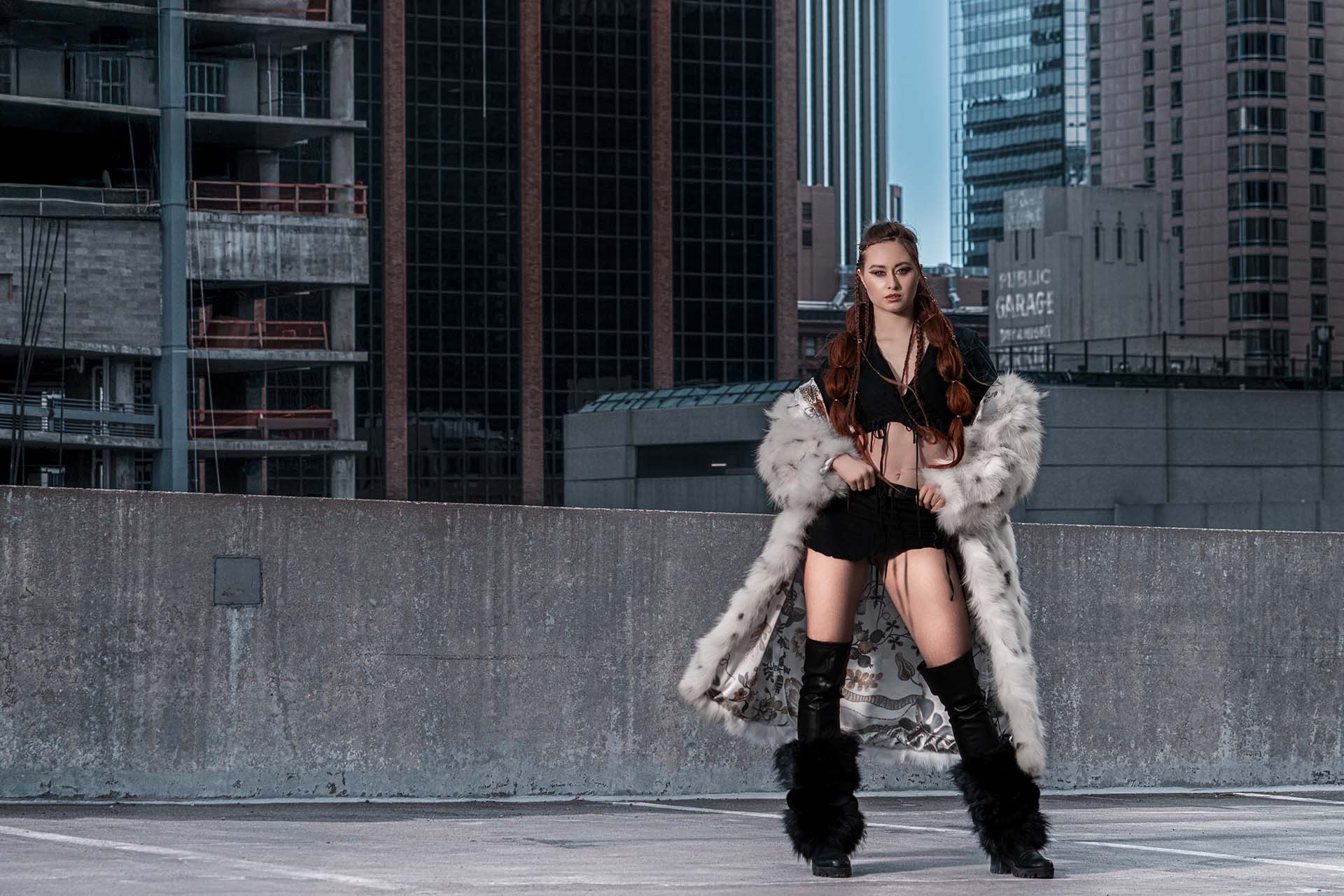 Model in a white fur coat standing on an urban rooftop with a city skyline backdrop