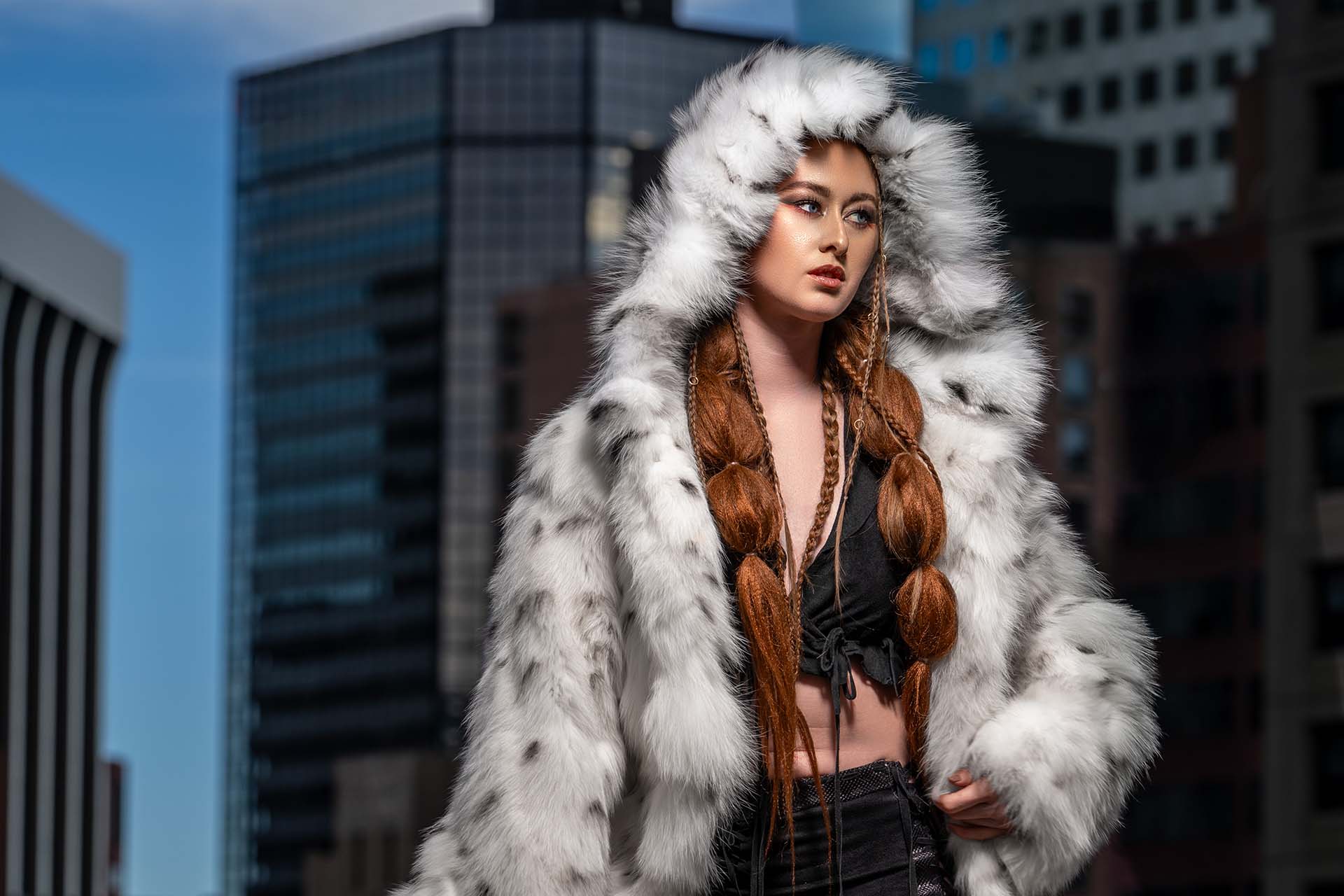 Close portrait of a model in a white fur coat with a city skyline backdrop