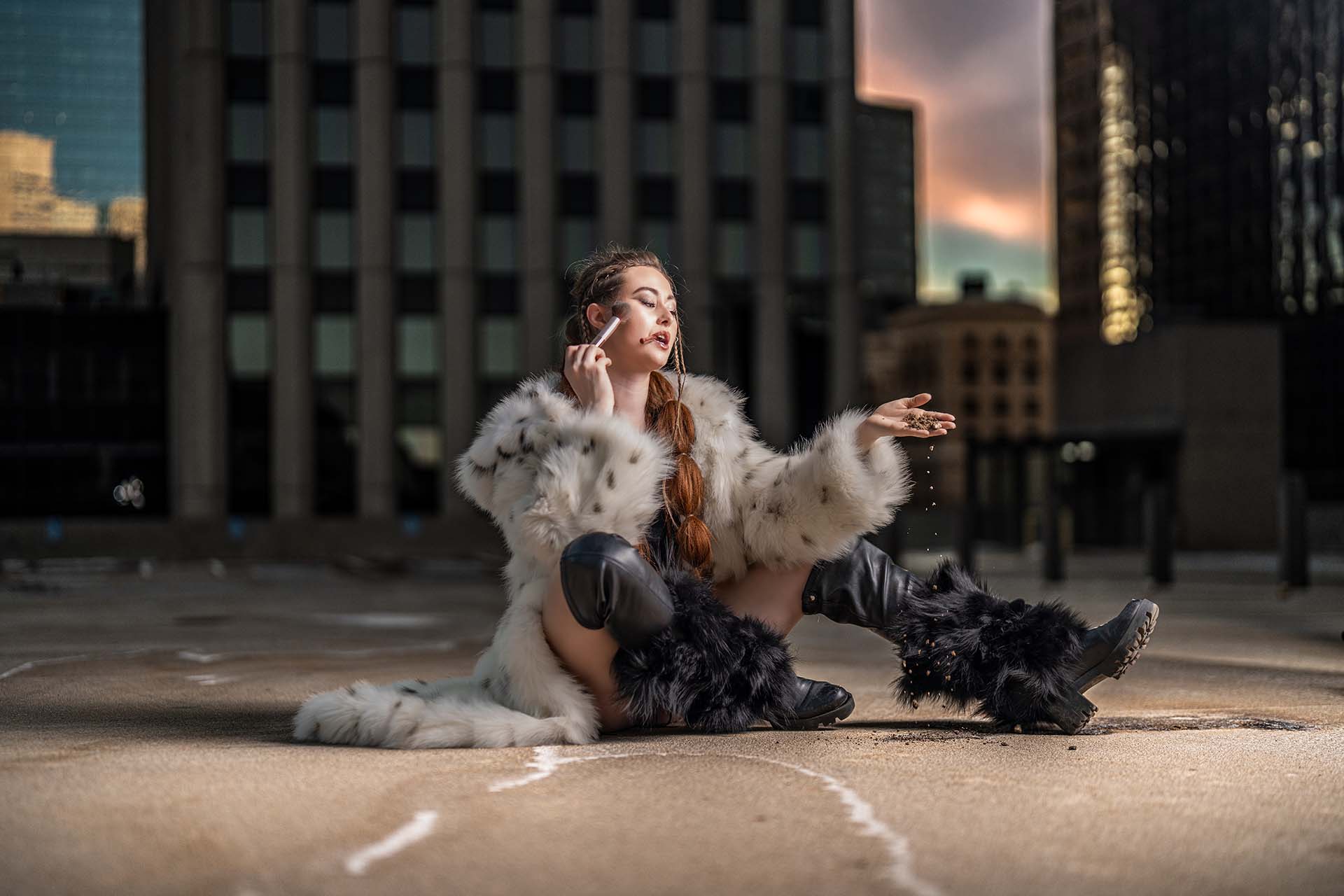 Model seated on the ground in a fur coat on an urban rooftop, editorial fashion photography