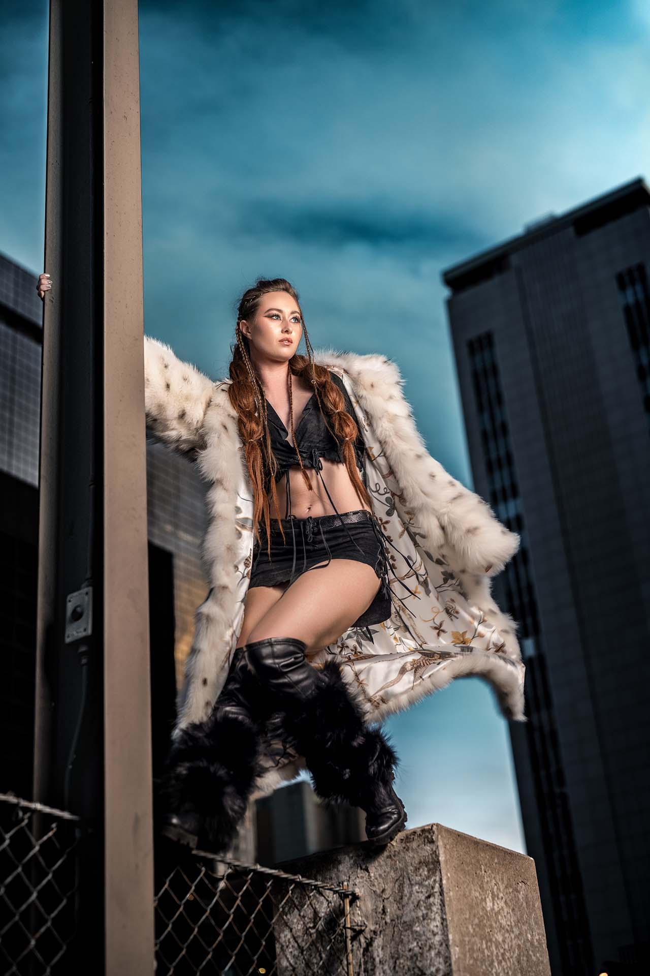Model standing on a ledge in a fur coat, dramatic sky and urban rooftop backdrop