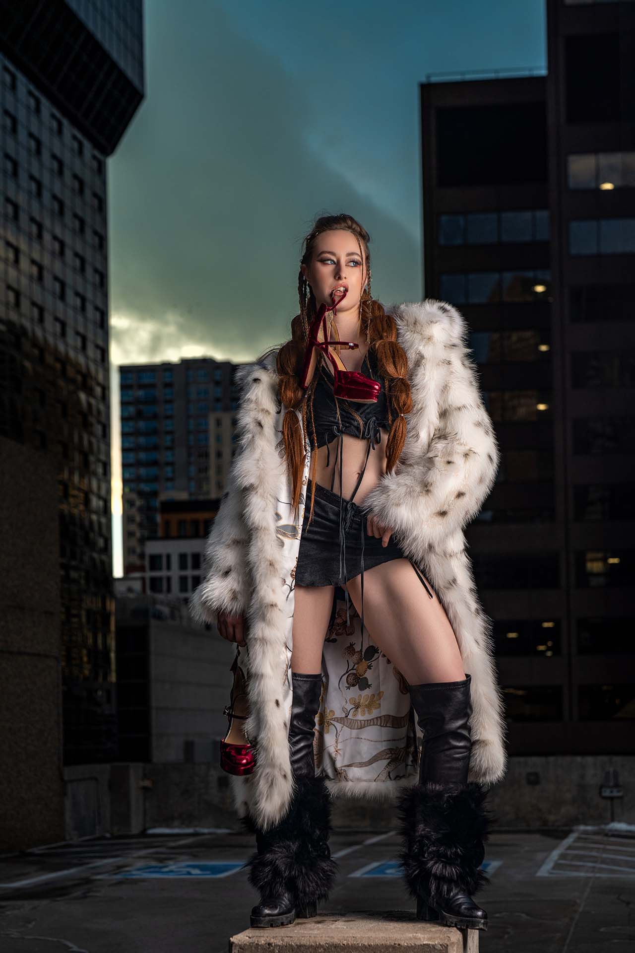 Model standing in a fur coat with a city skyline at dusk in the background