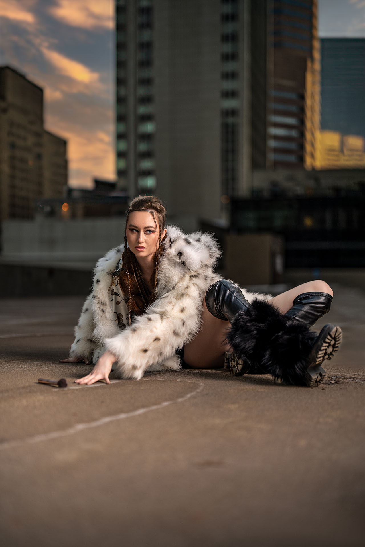 Model seated on the ground in a fur coat on an urban rooftop, alternate pose