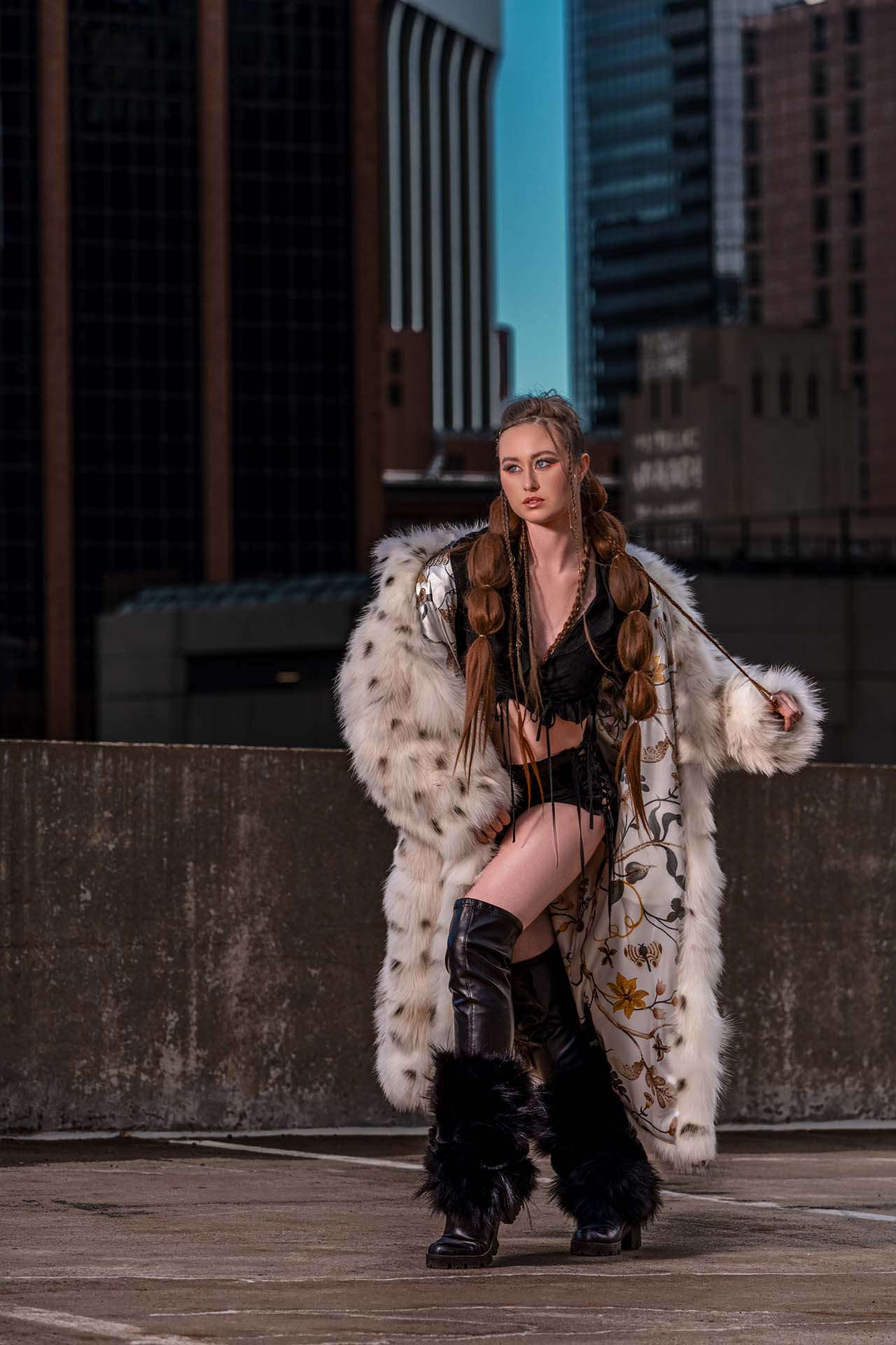 Model in a fur coat and boots standing on an urban rooftop, city skyline backdrop