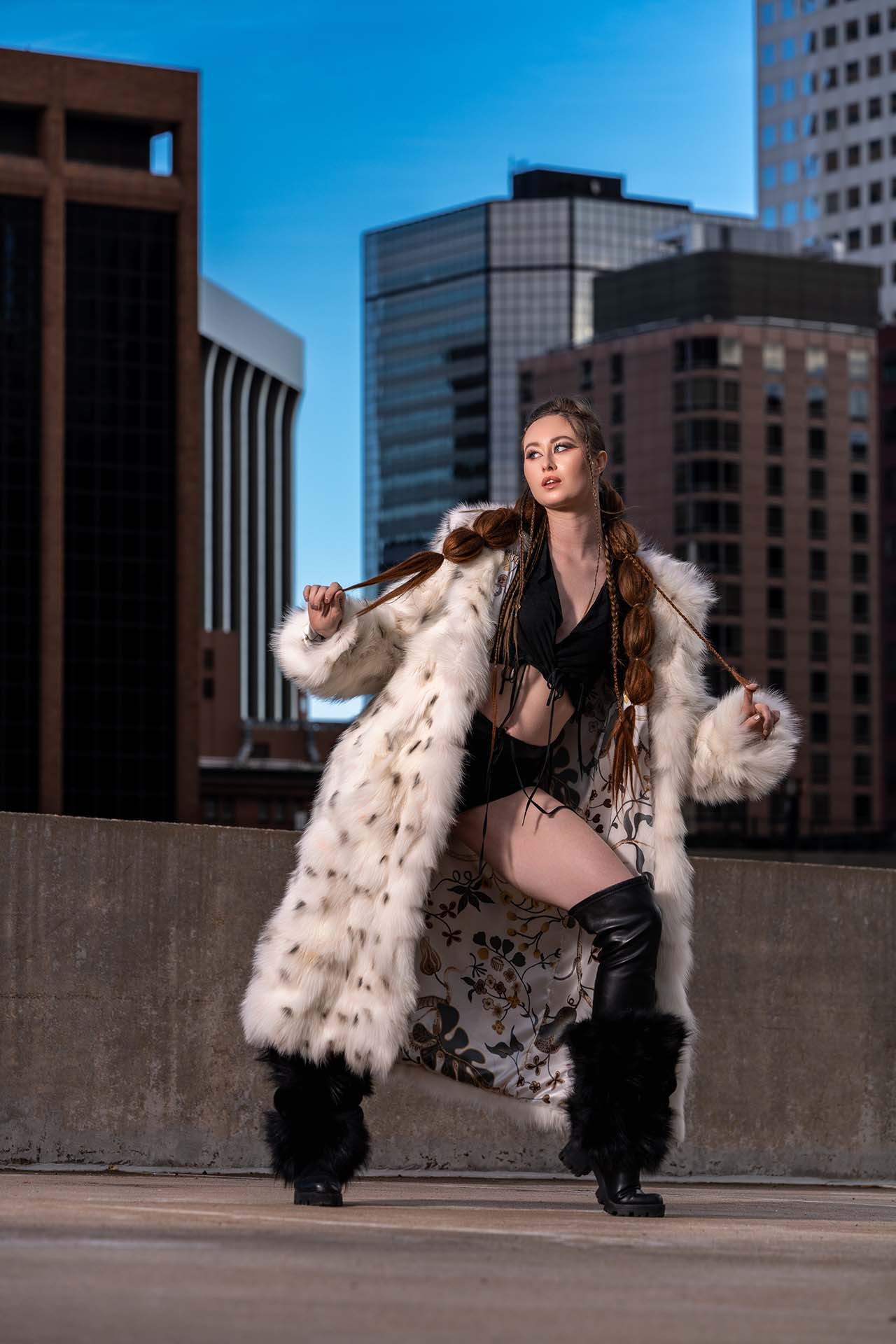 Model in a fur coat and boots in a dynamic pose on an urban rooftop