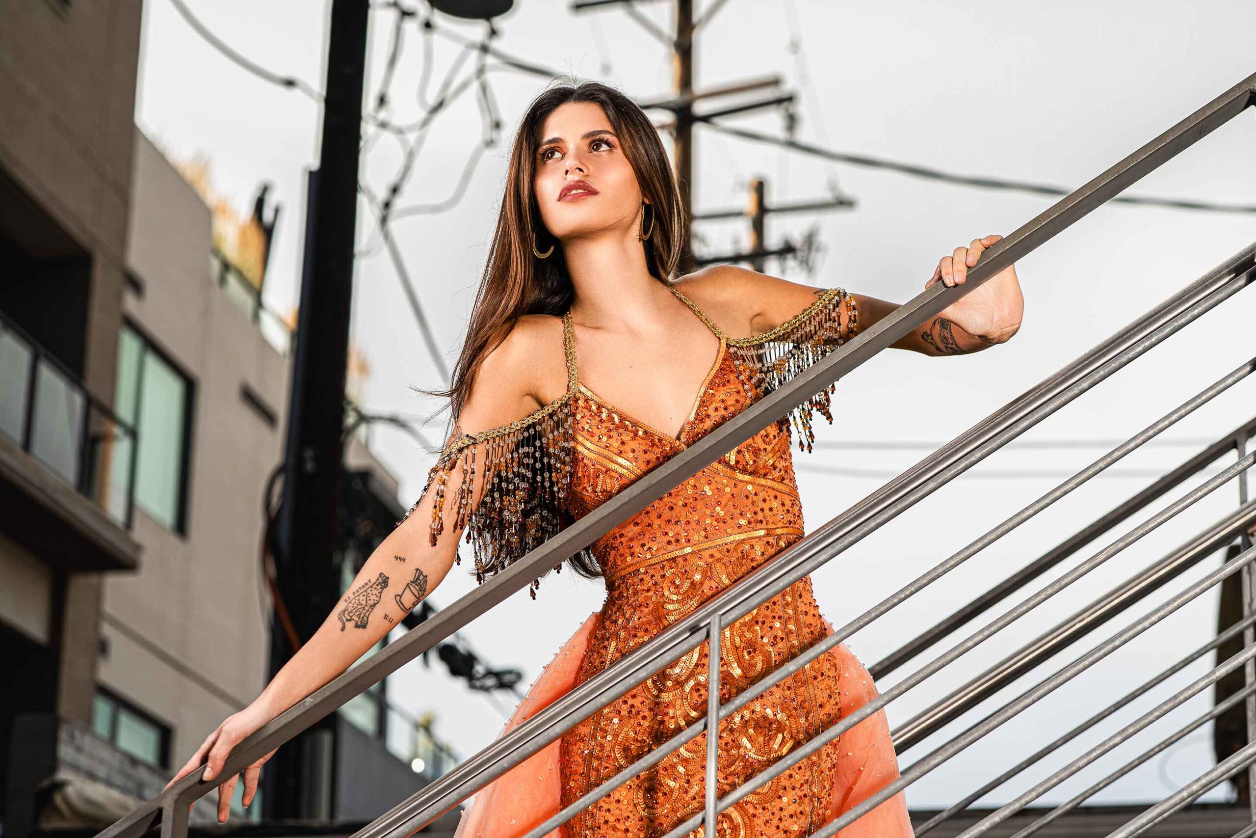 Adi Editorial Fashion Photography 06 Model in an orange gown posing against an urban railing with city buildings behind
