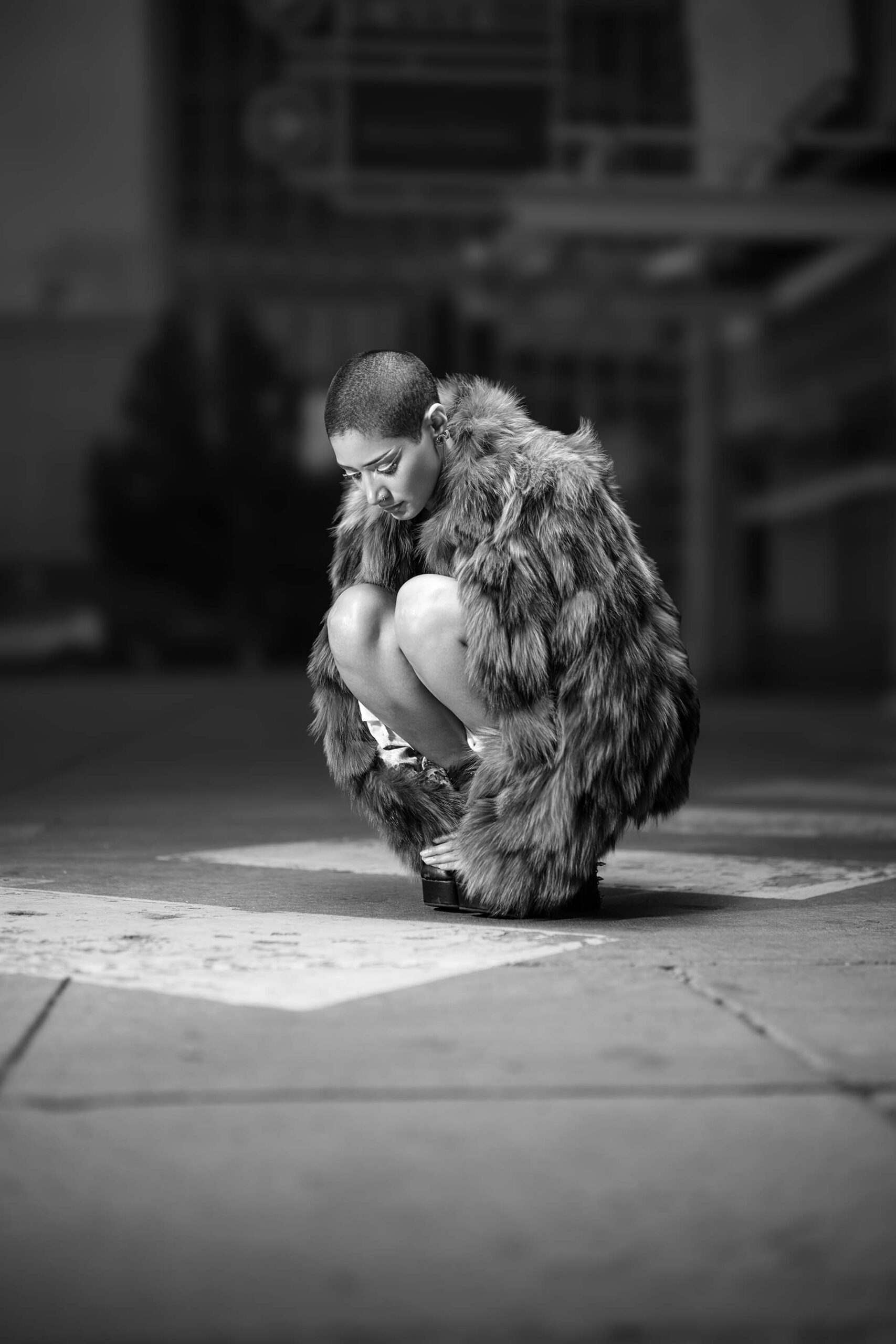 Black-and-white street photo of a model crouched in a styled fashion pose