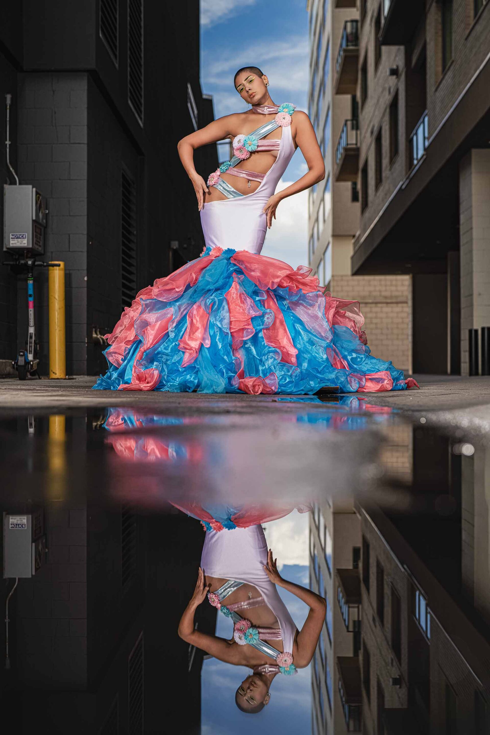 Model in a pink and teal ruffled gown on a wet reflective street, alternate pose, urban editorial photography