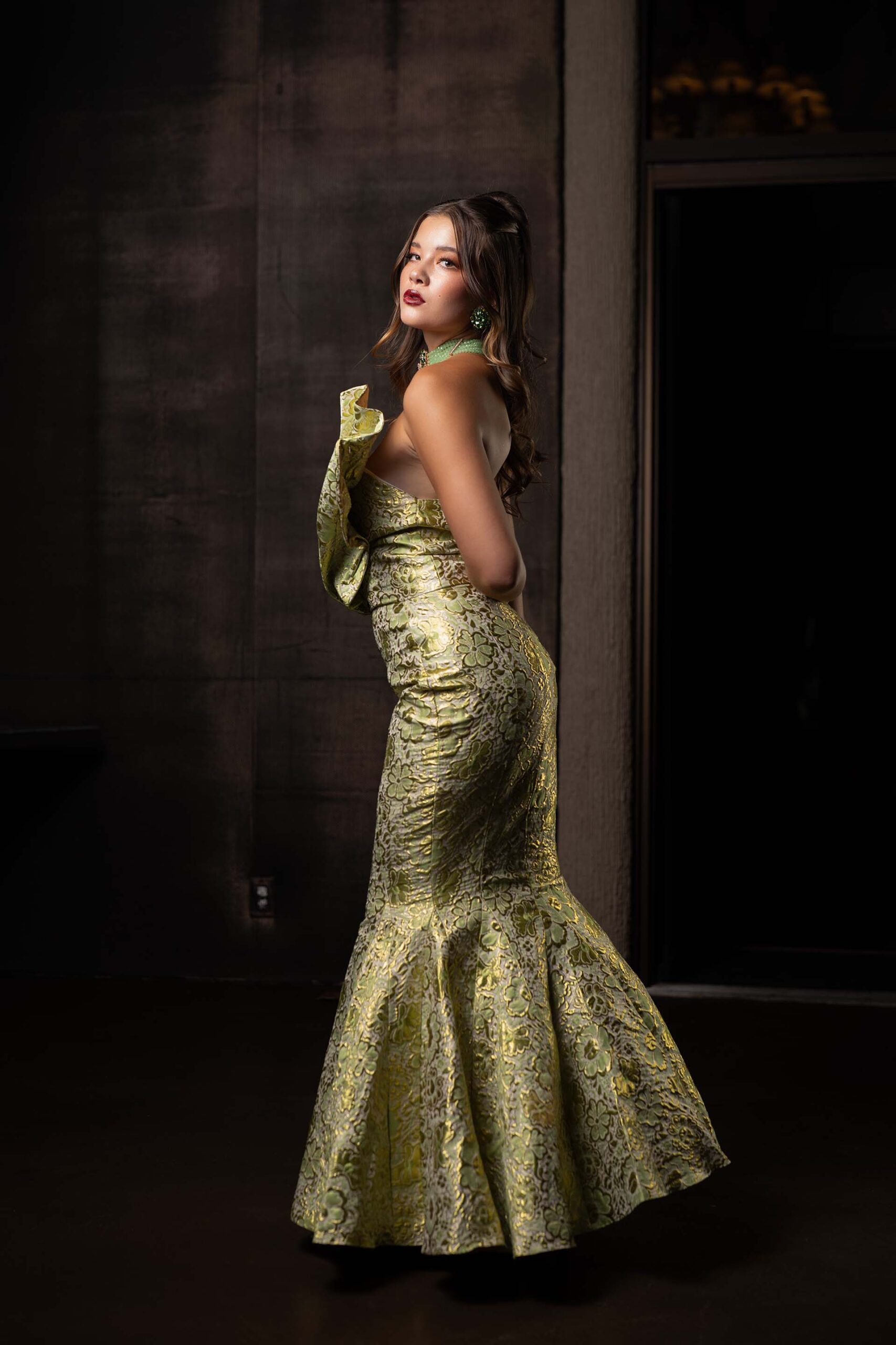 Model in a gold-green mermaid gown, side-profile formal portrait at the Cableland Venue