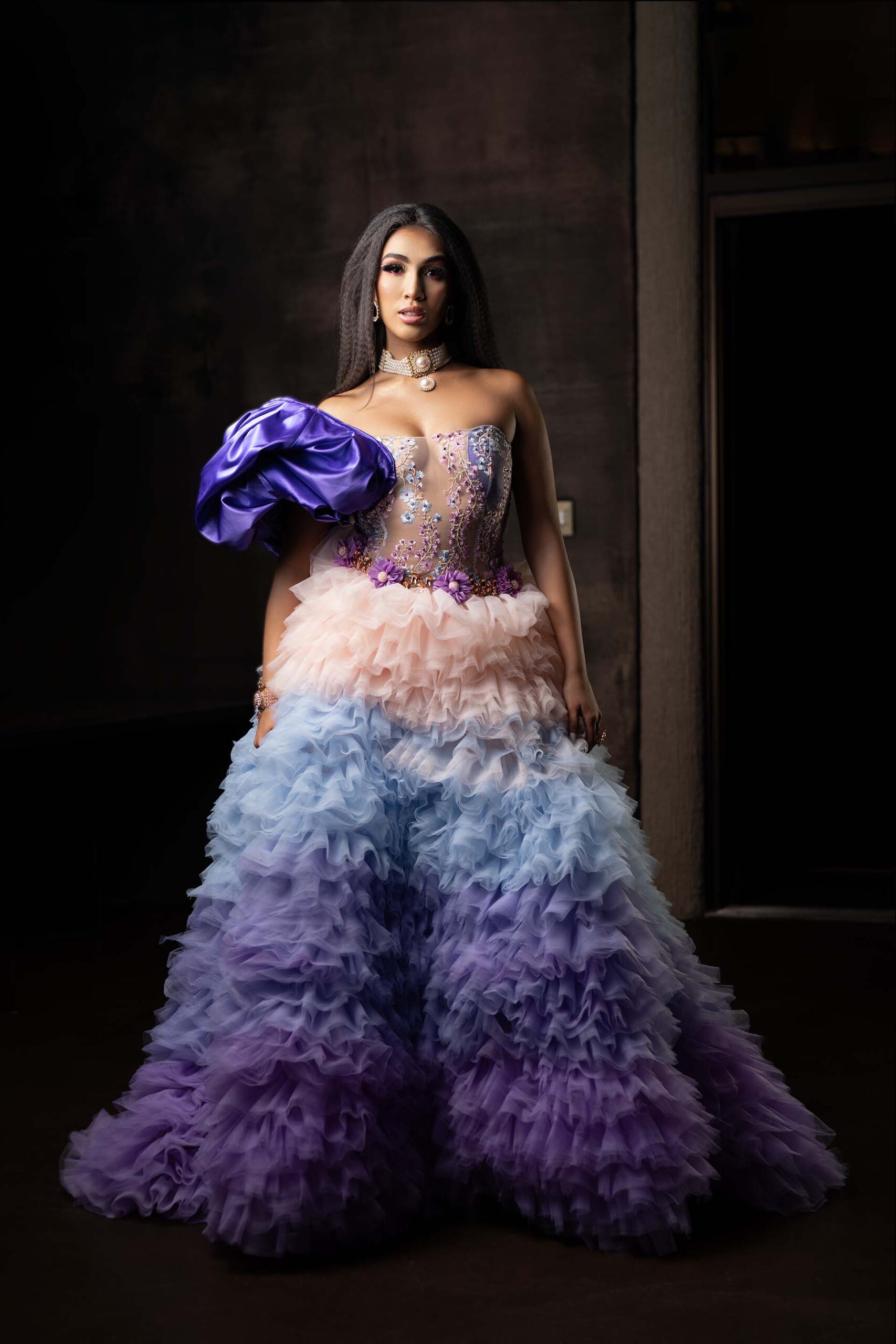 Model in a pink-to-blue ombre ruffled gown with a purple bow sleeve, formal portrait