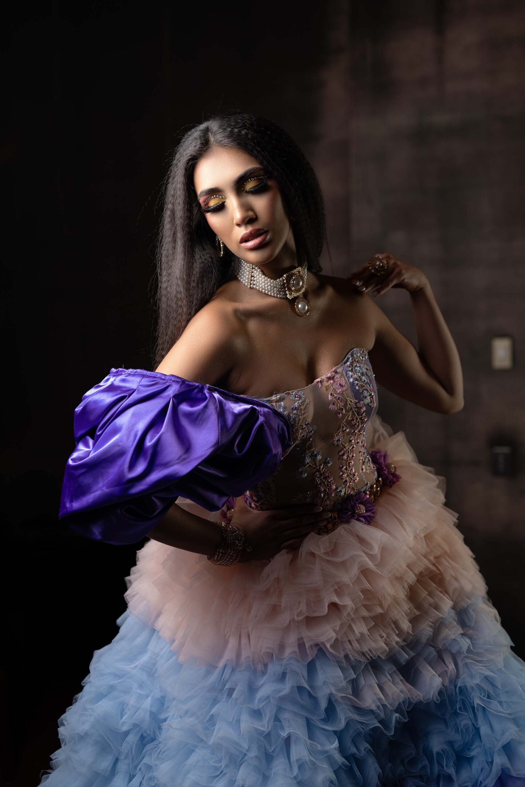 Model in a pink-to-blue ombre ruffled gown with a purple bow sleeve, alternate pose