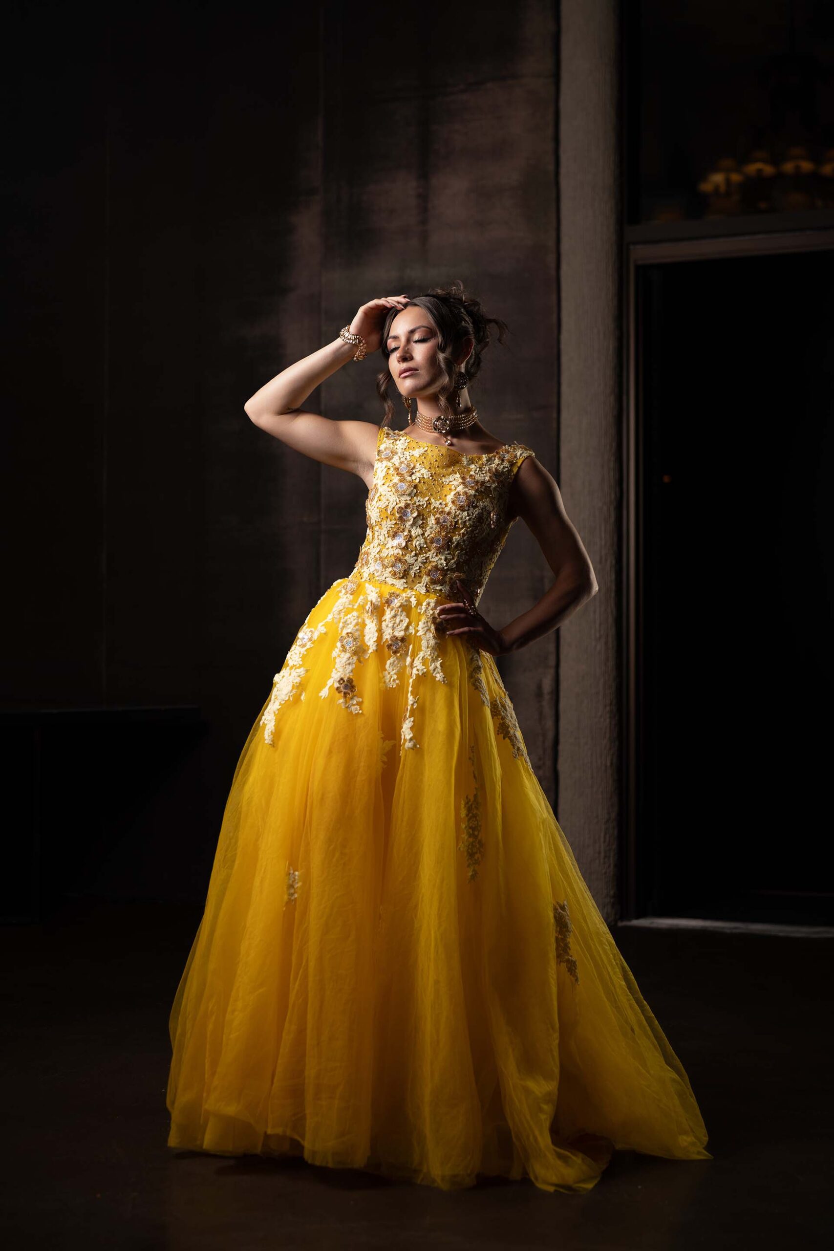 Model in a yellow tulle gown with a gold embellished bodice, hand near her head