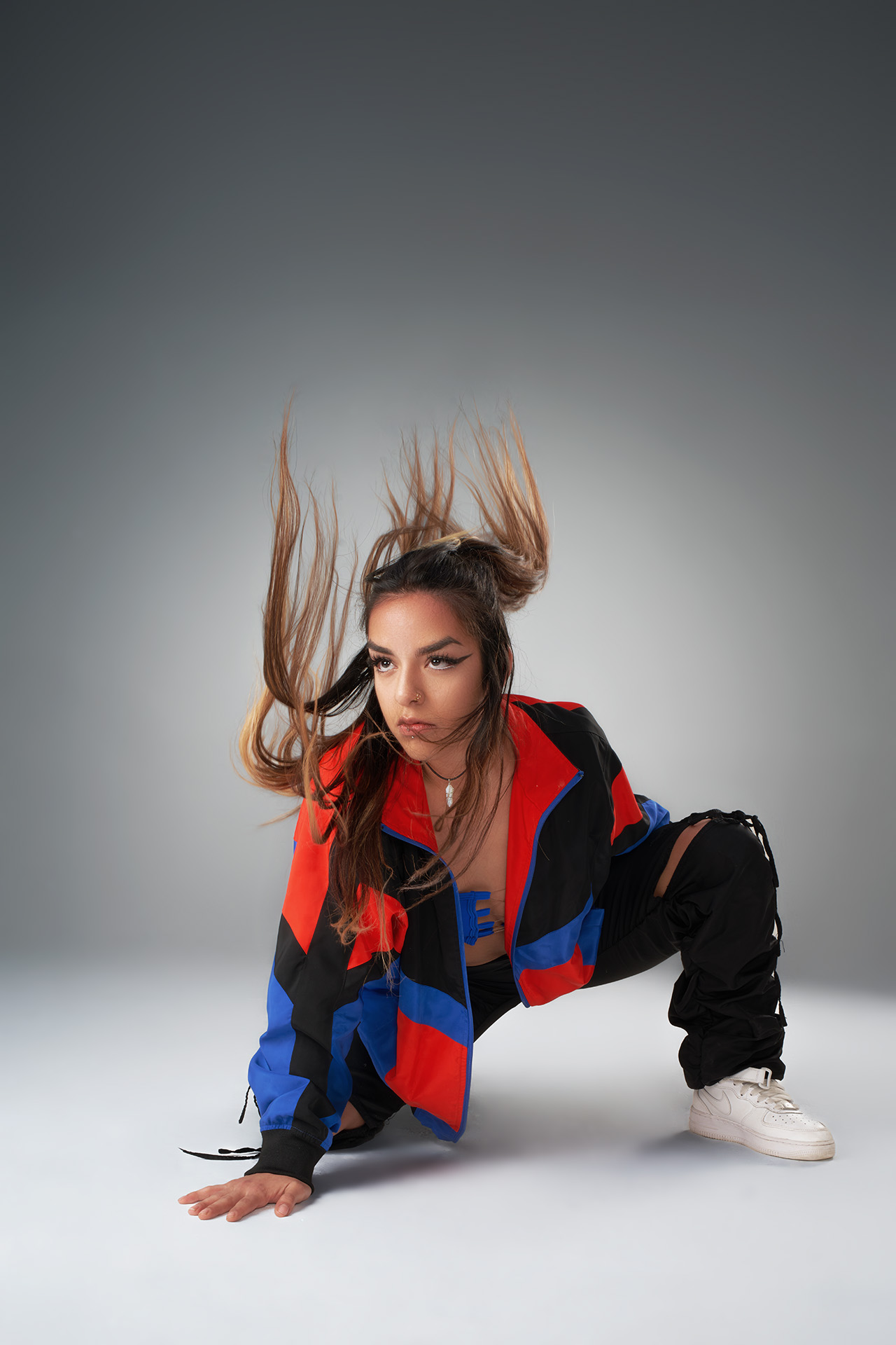 Dancer in a crouched pose with hair in motion, colorful patterned jacket, dynamic studio photography