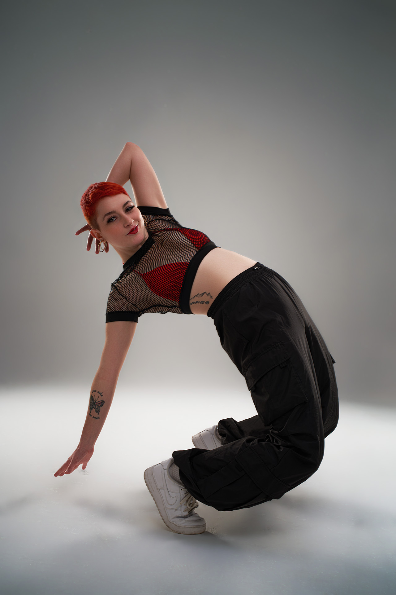 Dancer in a backbend pose wearing a red bra and mesh top, red hair, dynamic studio action photography