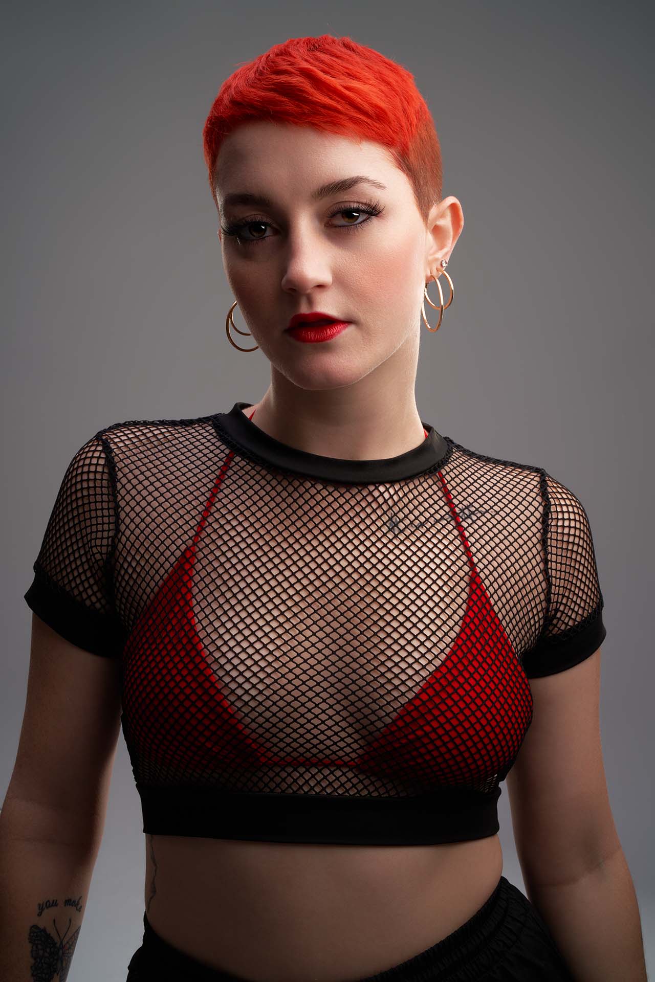 Dancer with bright red hair in a red bra and mesh crop top, studio portrait photography