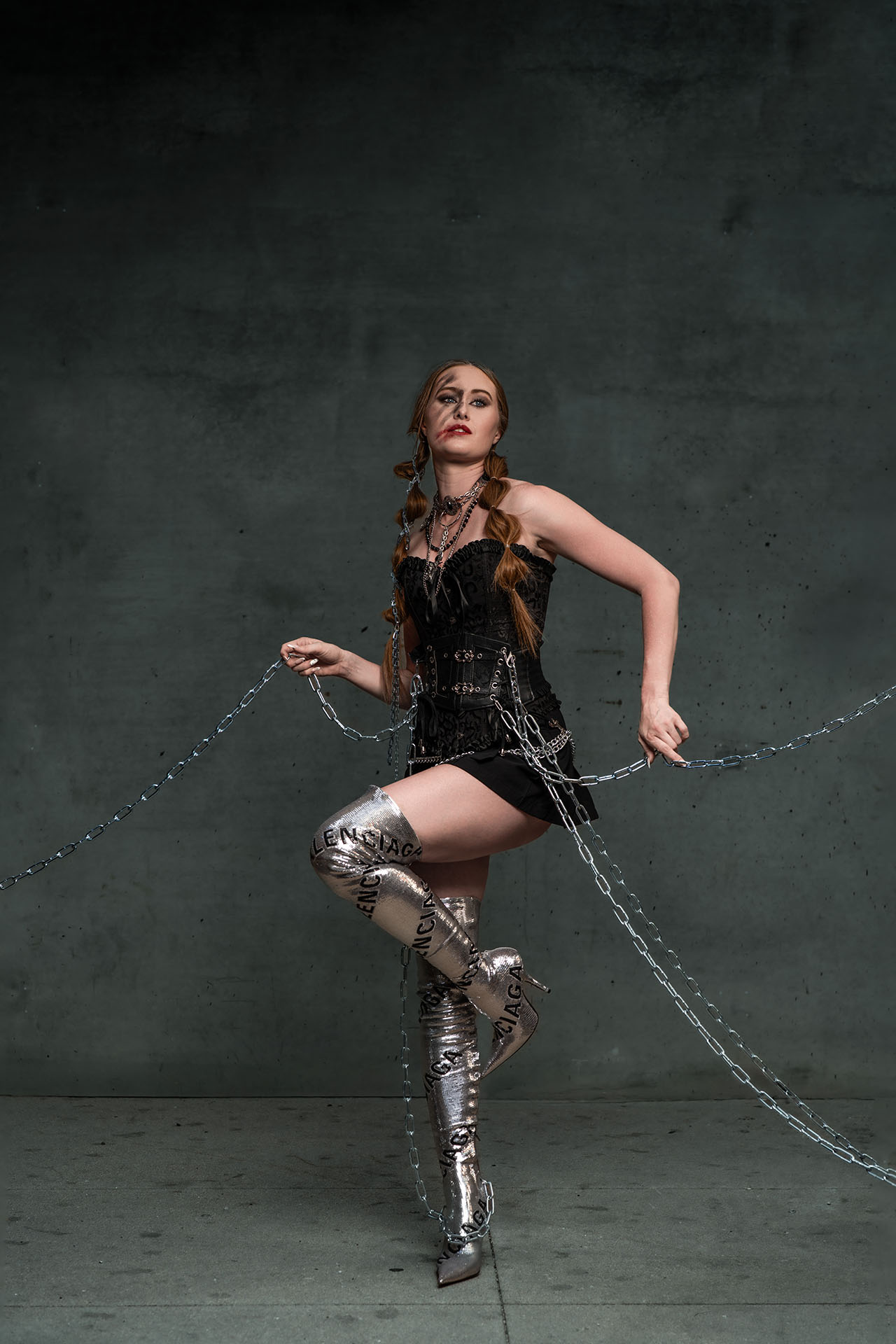 Full-body editorial photo of a model in a black outfit with a chain, dynamic pose against a concrete backdrop