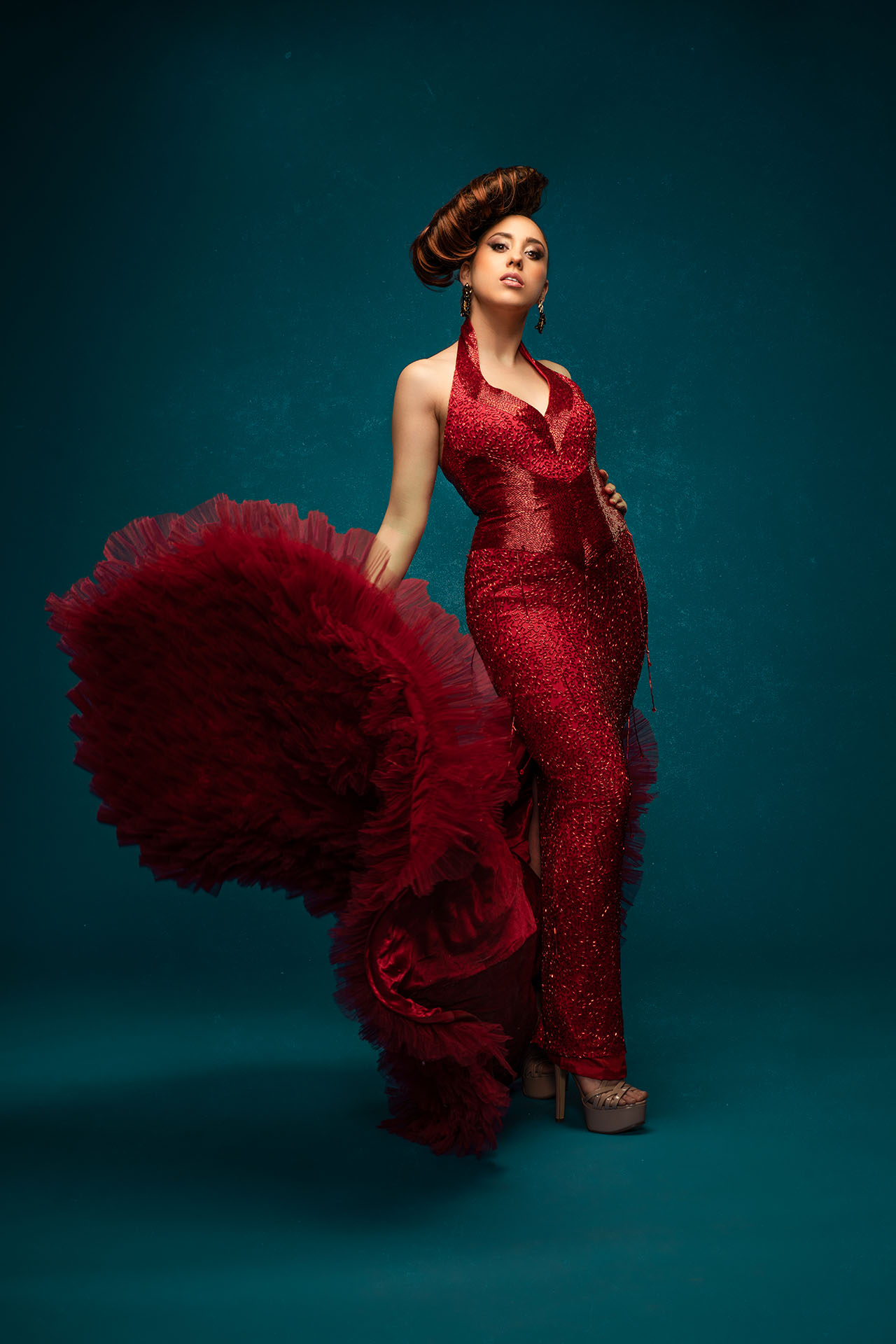 Model in a deep red ruffled gown with a dramatic sleeve, teal studio backdrop