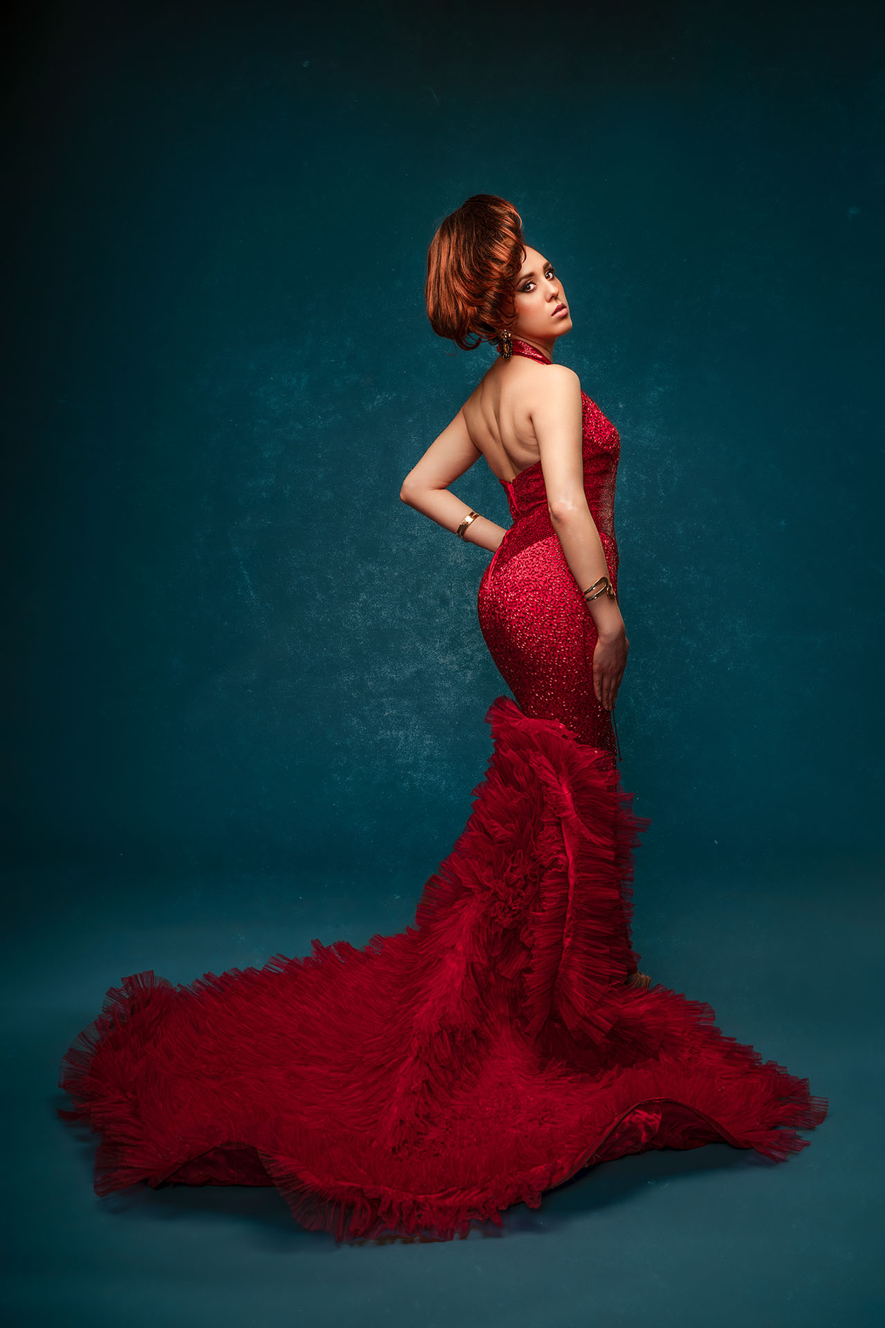 Model in a deep red mermaid-style gown with a dramatic train, side profile pose